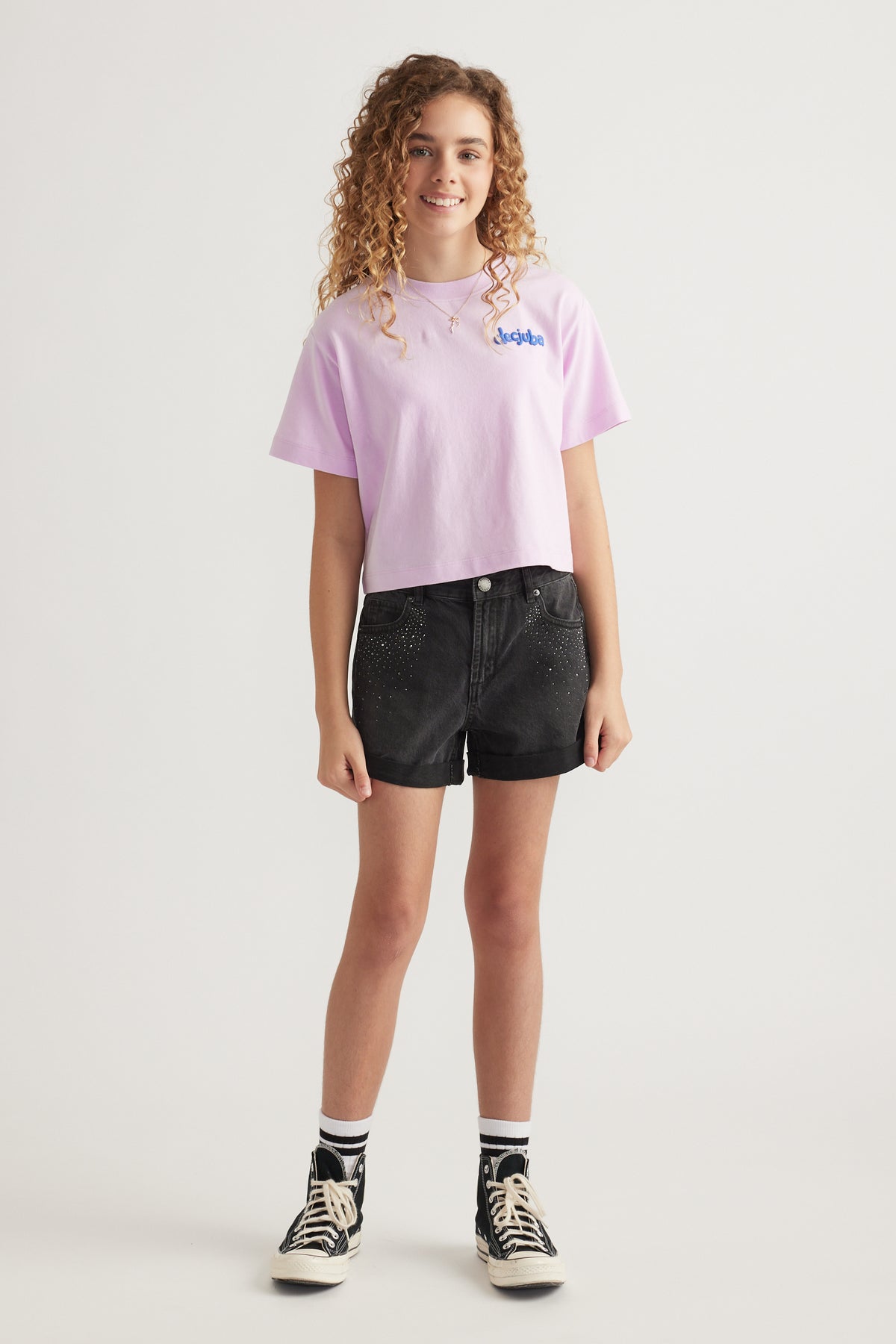Girl wearing a pink graphic tee with black rhinestone denim shorts and high top sneakers
