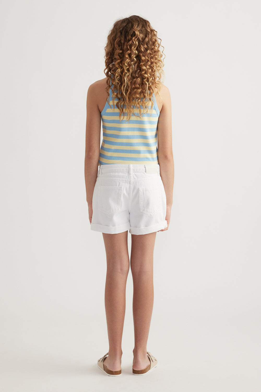 Girl viewed from behind wearing white denim shorts, a blue striped tank top and sandals