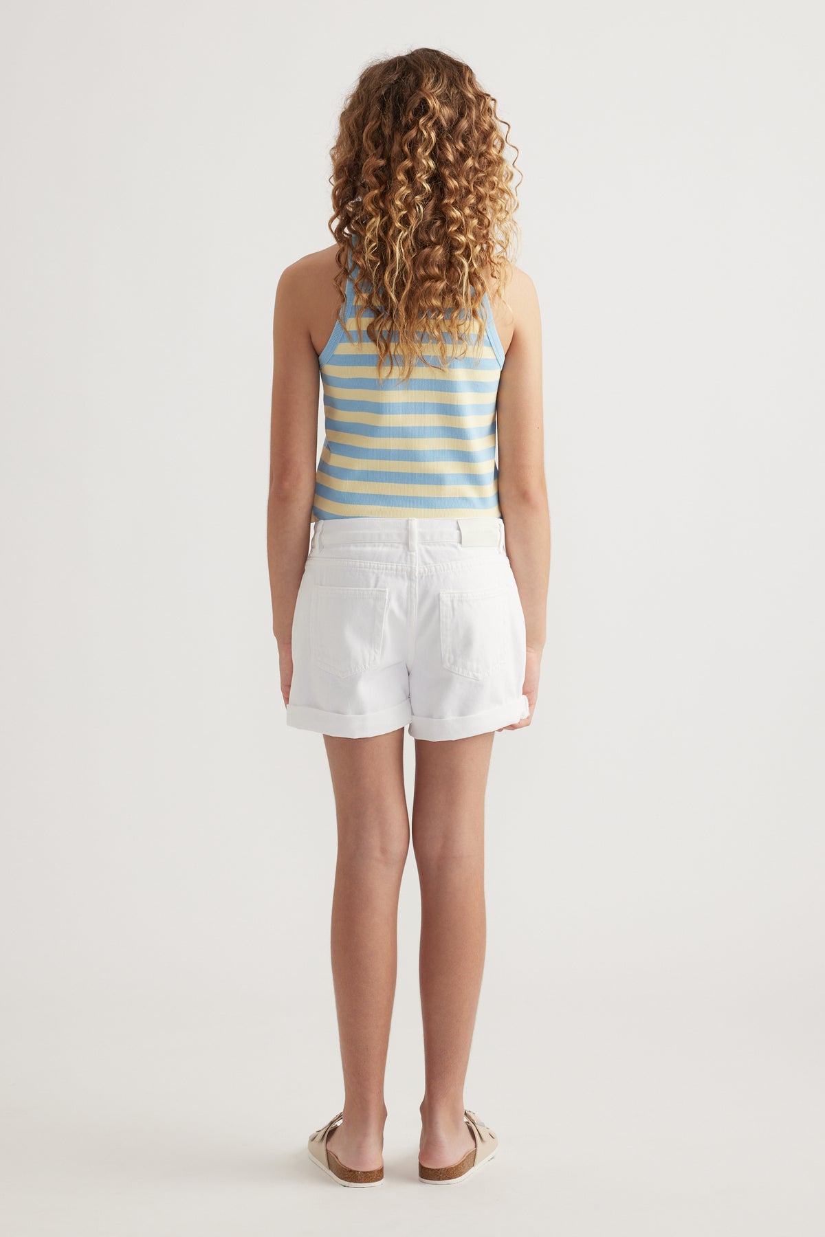 Girl viewed from behind wearing white denim shorts, a blue striped tank top and sandals
