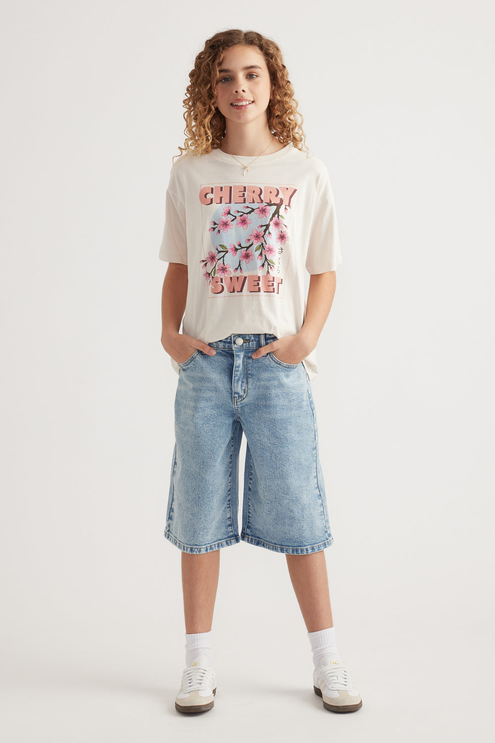Girl wearing an oversized white graphic tee with denim knee-length shorts and sneakers
