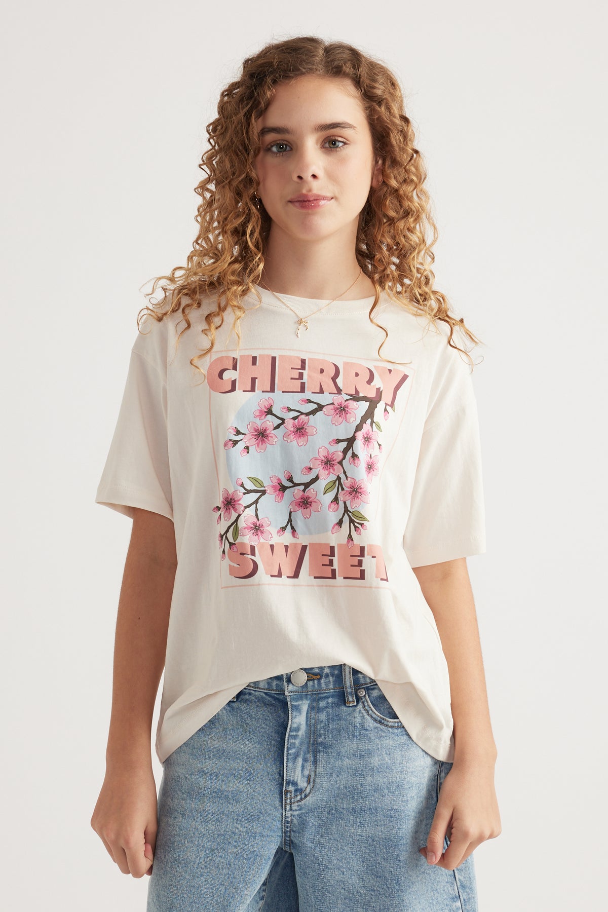 Girl wearing an oversized cream graphic tee with cherry blossom print and blue jeans