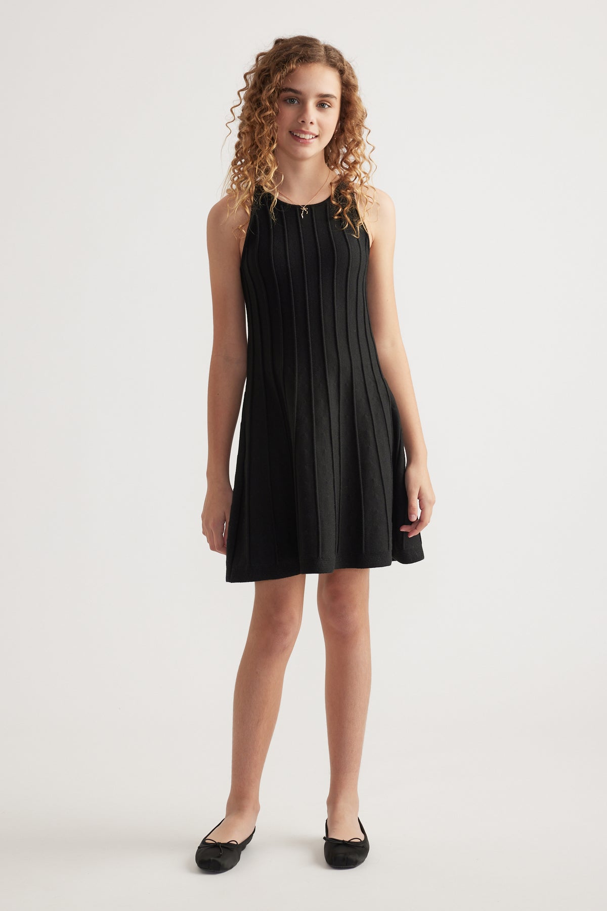 Girl wearing a black sleeveless knit fit and flare dress with panelled detailing and black flats