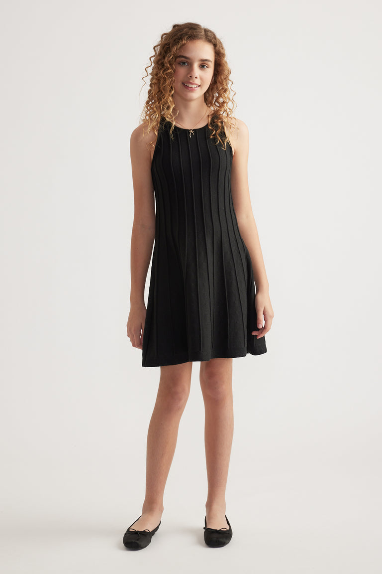 Girl wearing a black sleeveless knit fit and flare dress with panelled detailing and black flats