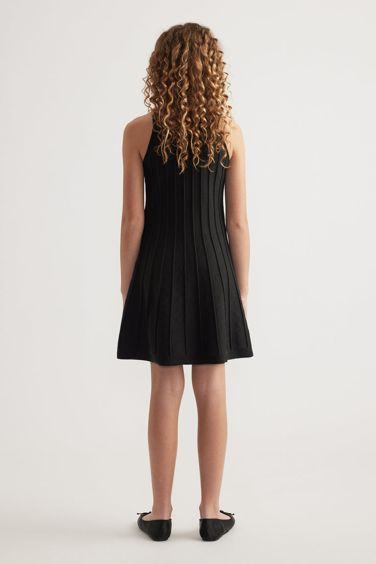Girl seen from behind wearing a black sleeveless knit fit and flare mini dress with black flats