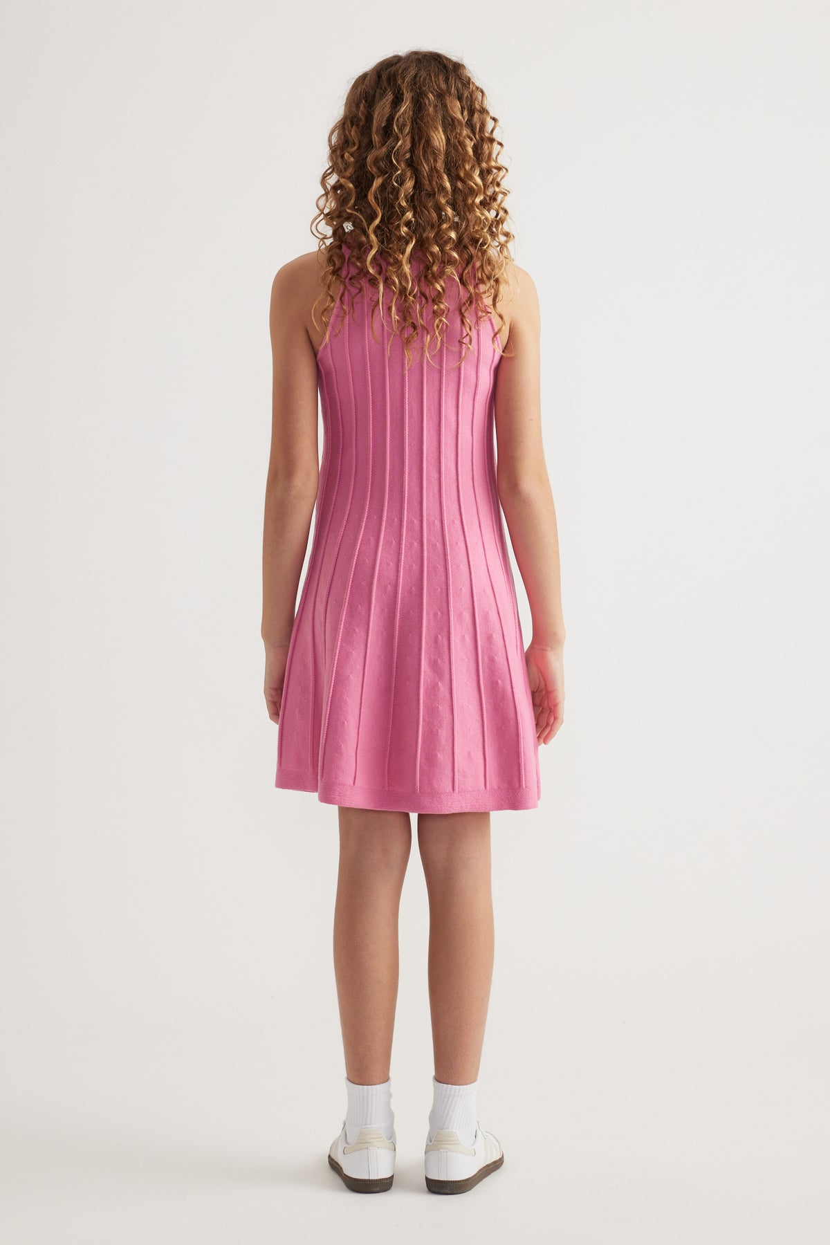 Girl seen from behind wearing a pink sleeveless knit fit and flare mini dress with panelled detailing