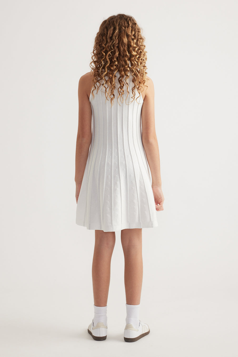 Girl seen from behind wearing a white sleeveless knit fit and flare mini dress with socks and sneakers