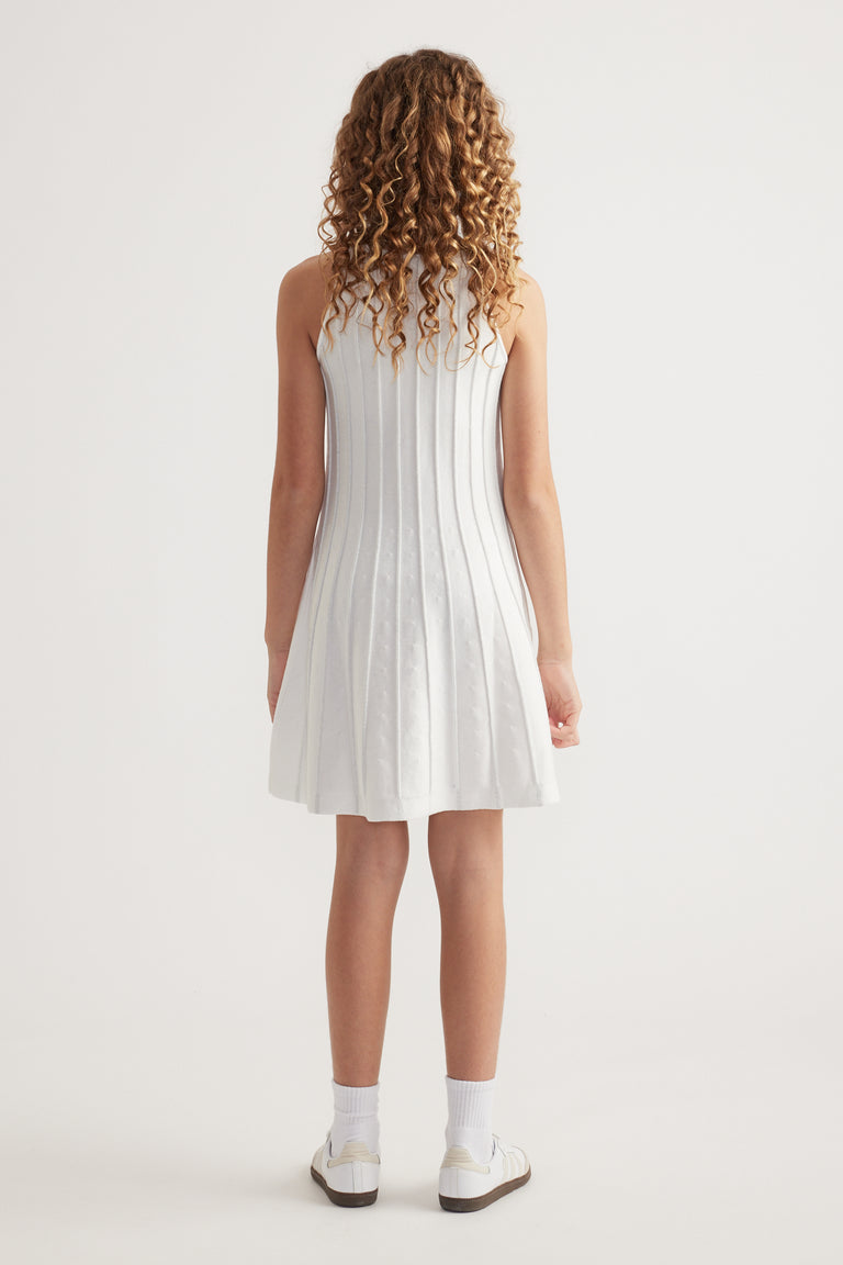 Girl seen from behind wearing a white sleeveless knit fit and flare mini dress with socks and sneakers