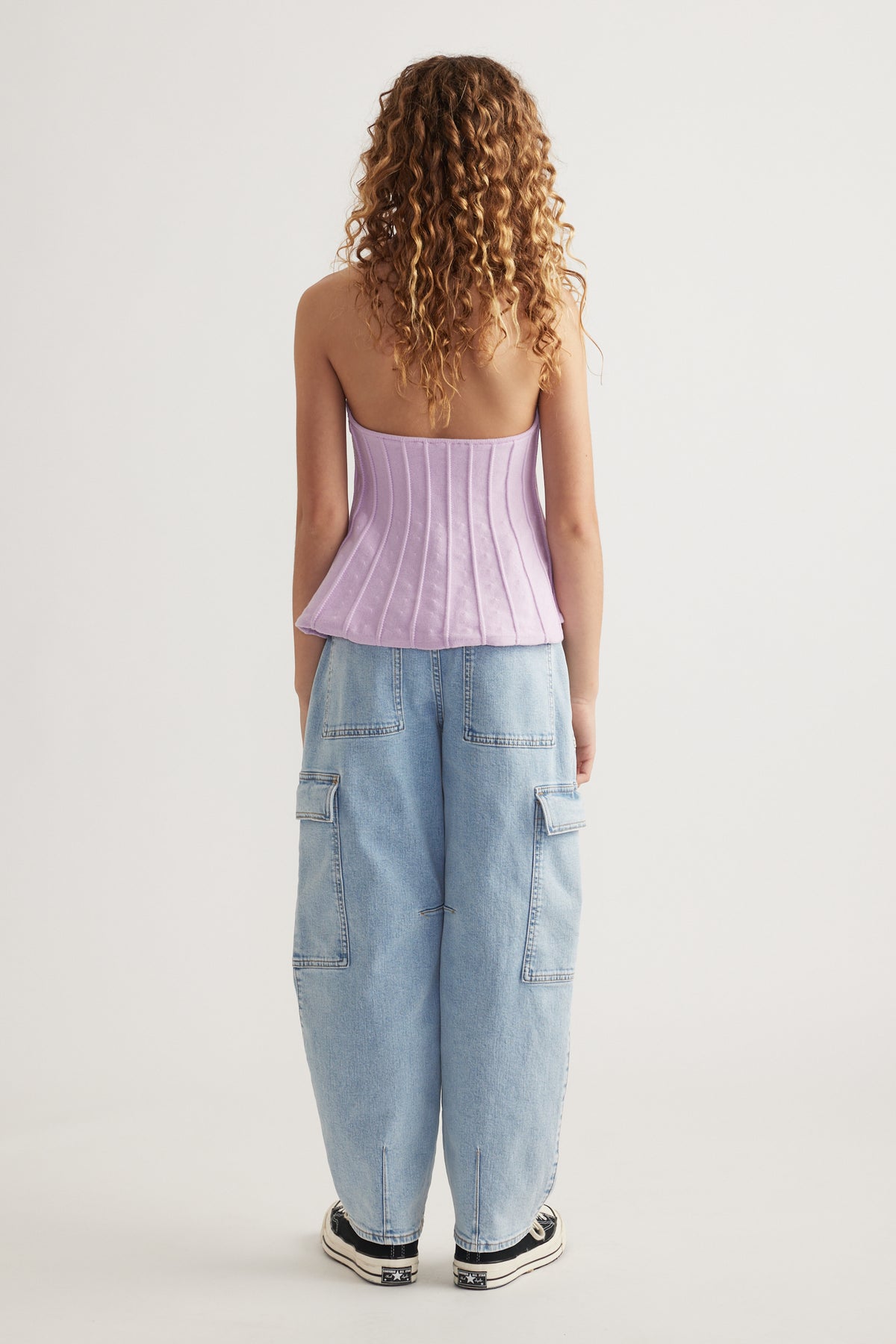 Back view of a girl wearing a lavender halter top, light blue cargo jeans and black sneakers