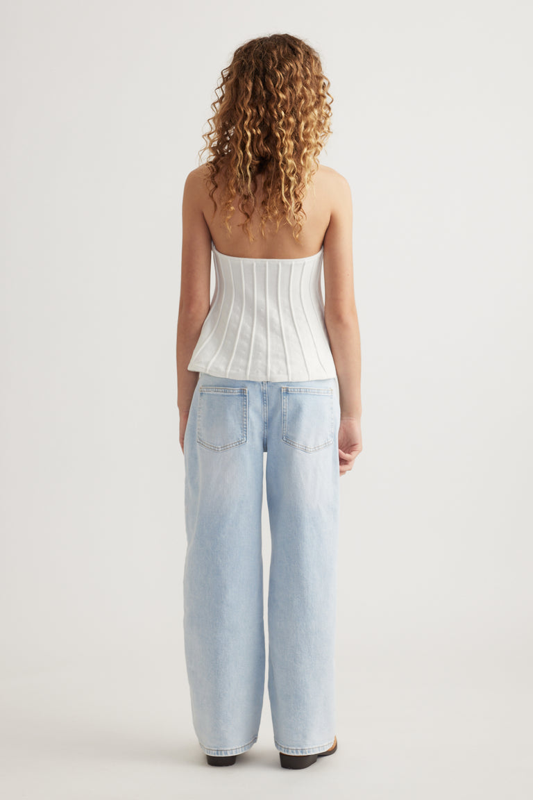 Back view of a girl wearing a white halter top with light blue wide leg jeans and black shoes