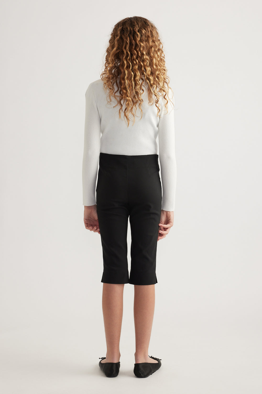 Girl wearing black high rise capri pants with a white ribbed sweater