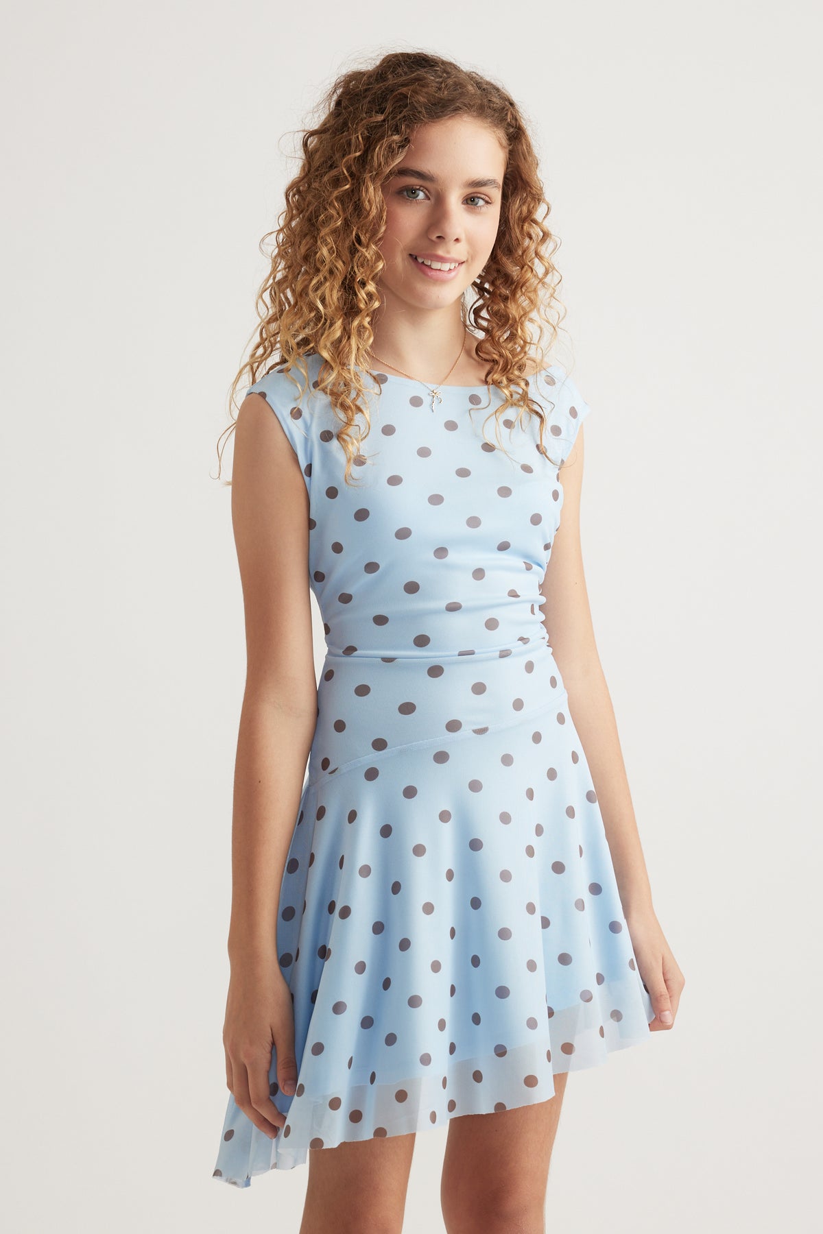 Girl wearing a light blue polka dot dress with a ruched waist and asymmetric hem
