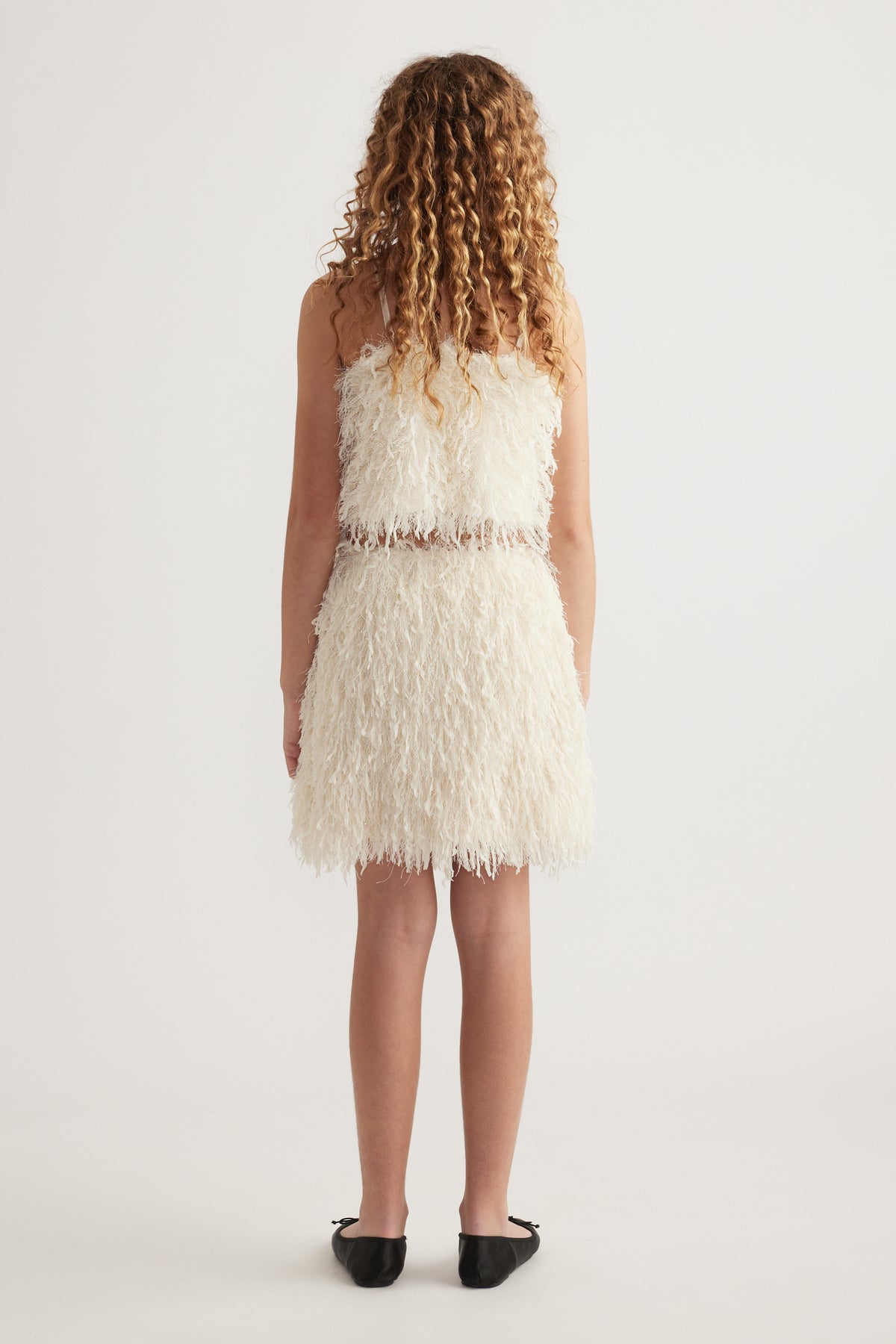 Back view of a girl wearing a cream textured skirt with an elasticated waist and black shoes