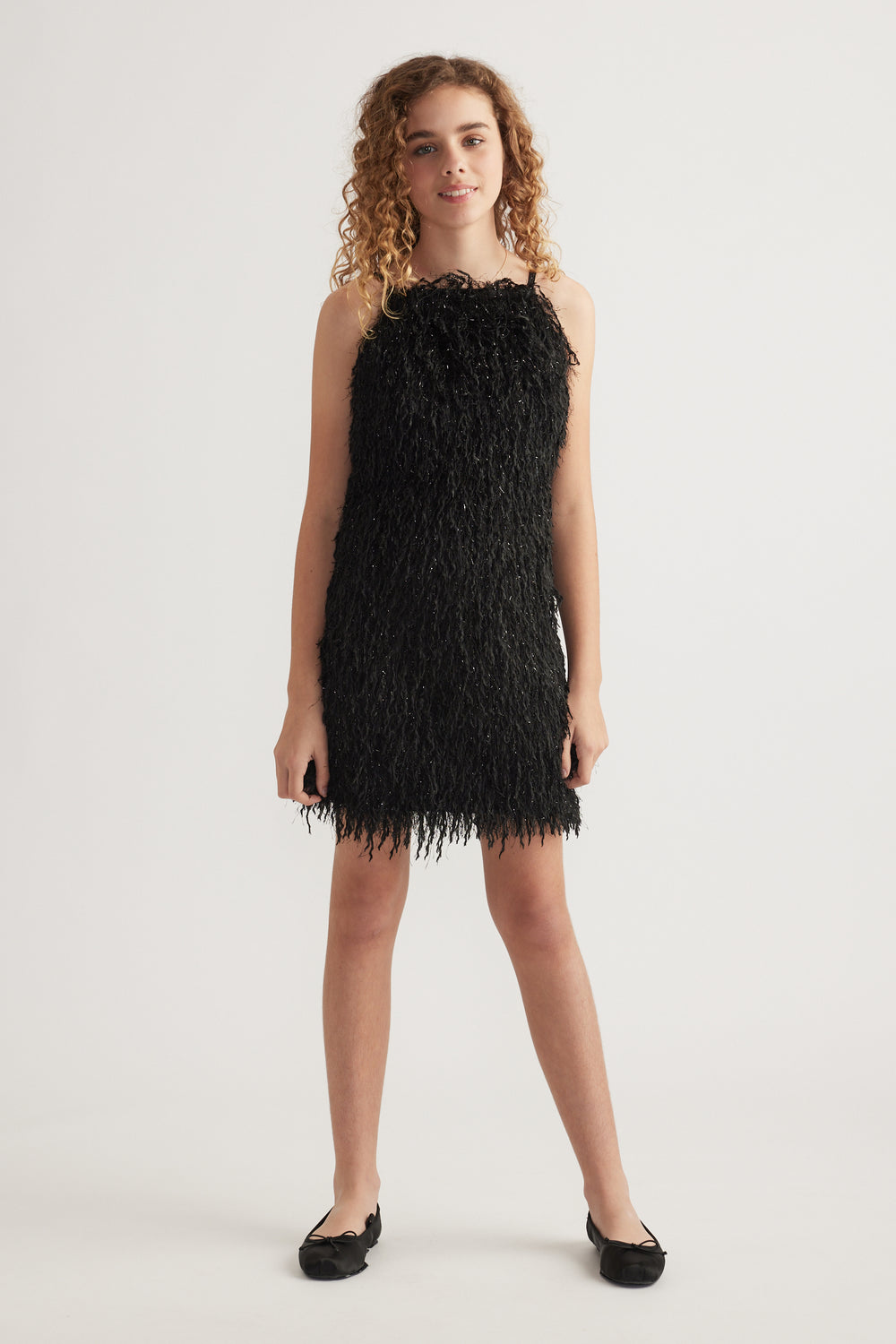Girl wearing a black textured sleeveless mini dress with thin straps and black flats