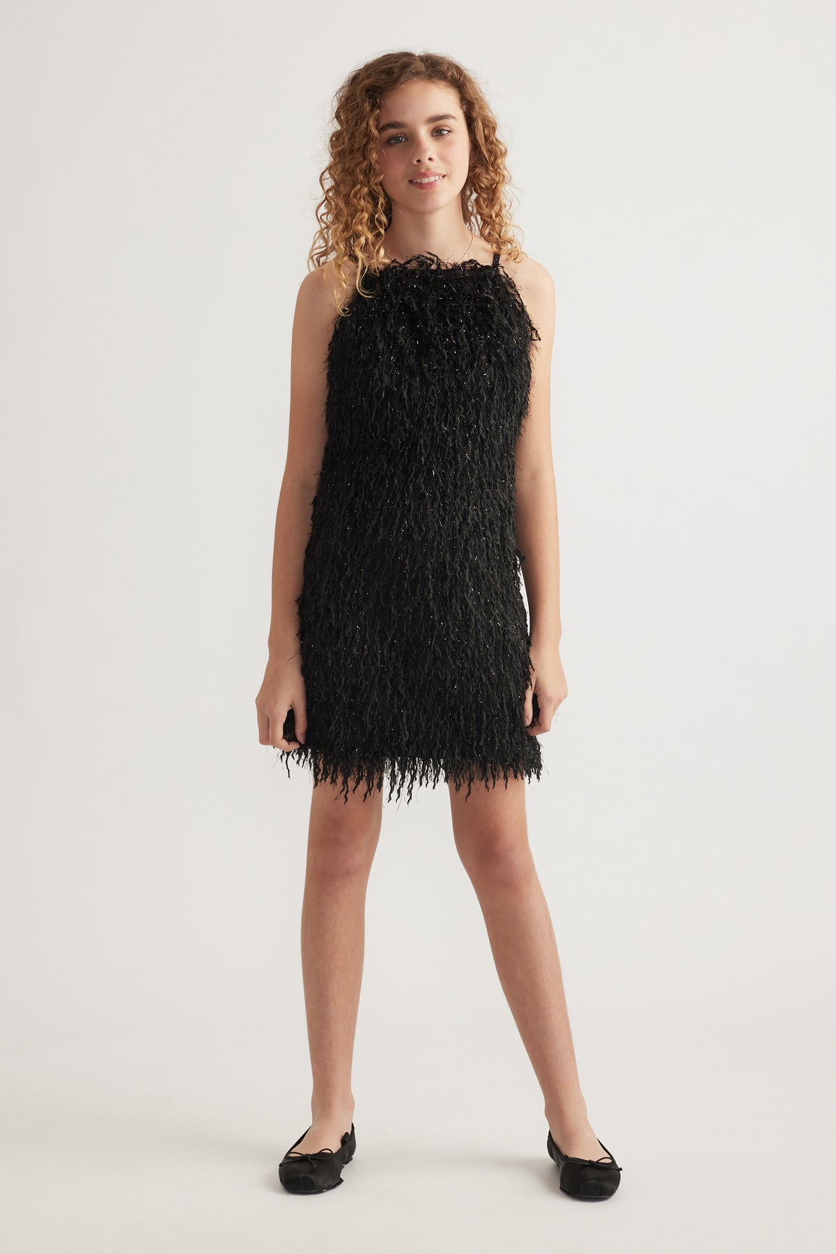 Girl wearing a black textured sleeveless mini dress with thin straps and black flats