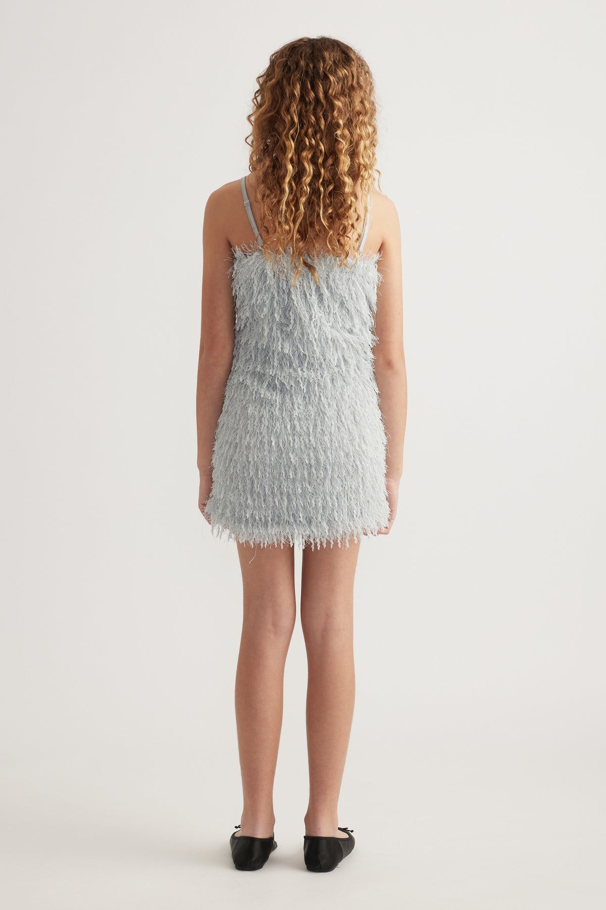 Back view of a girl wearing a light blue textured sleeveless mini dress with thin straps and black shoes