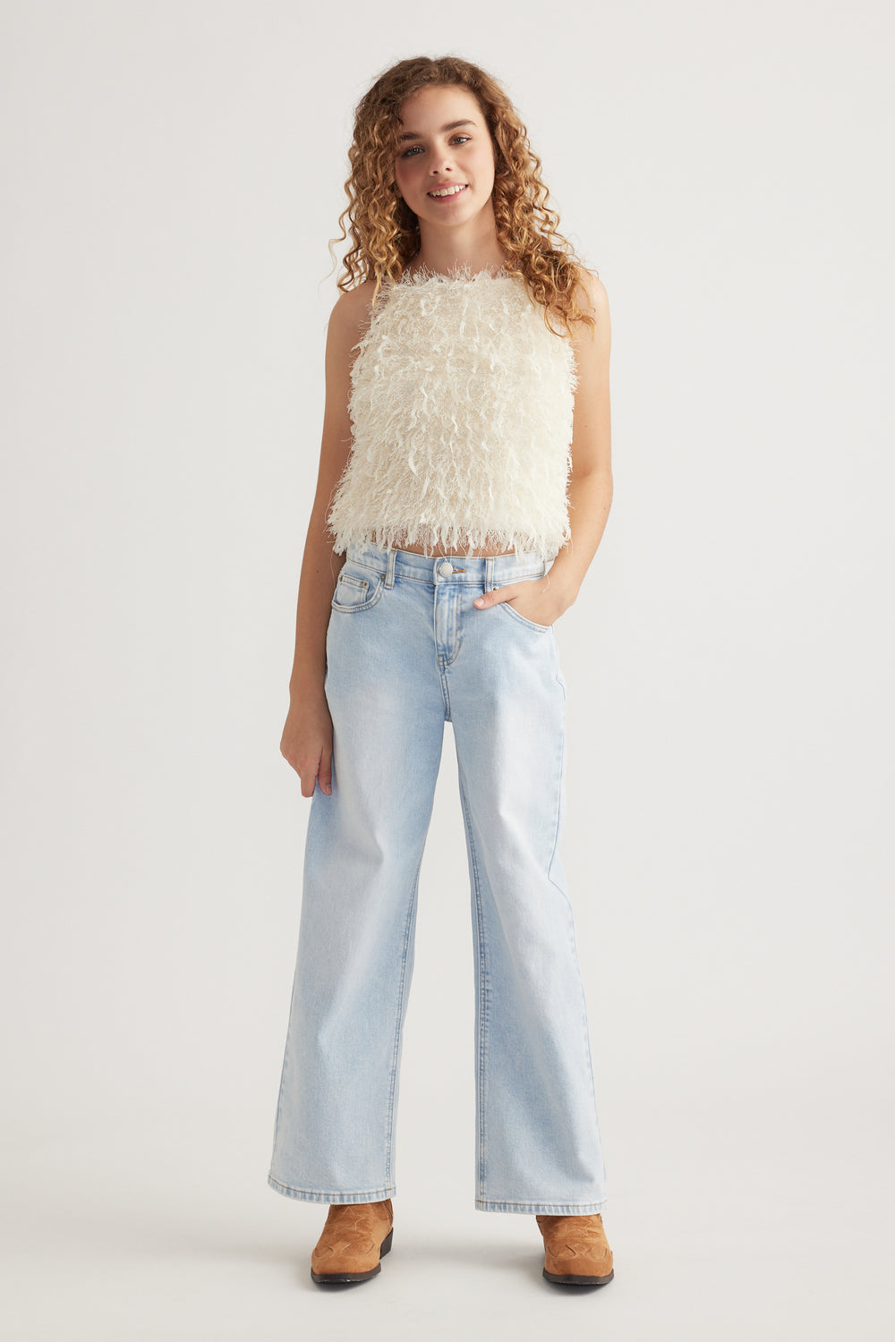 Girl wearing a cream textured sleeveless top with fringe, light blue wide-leg jeans and brown ankle boots