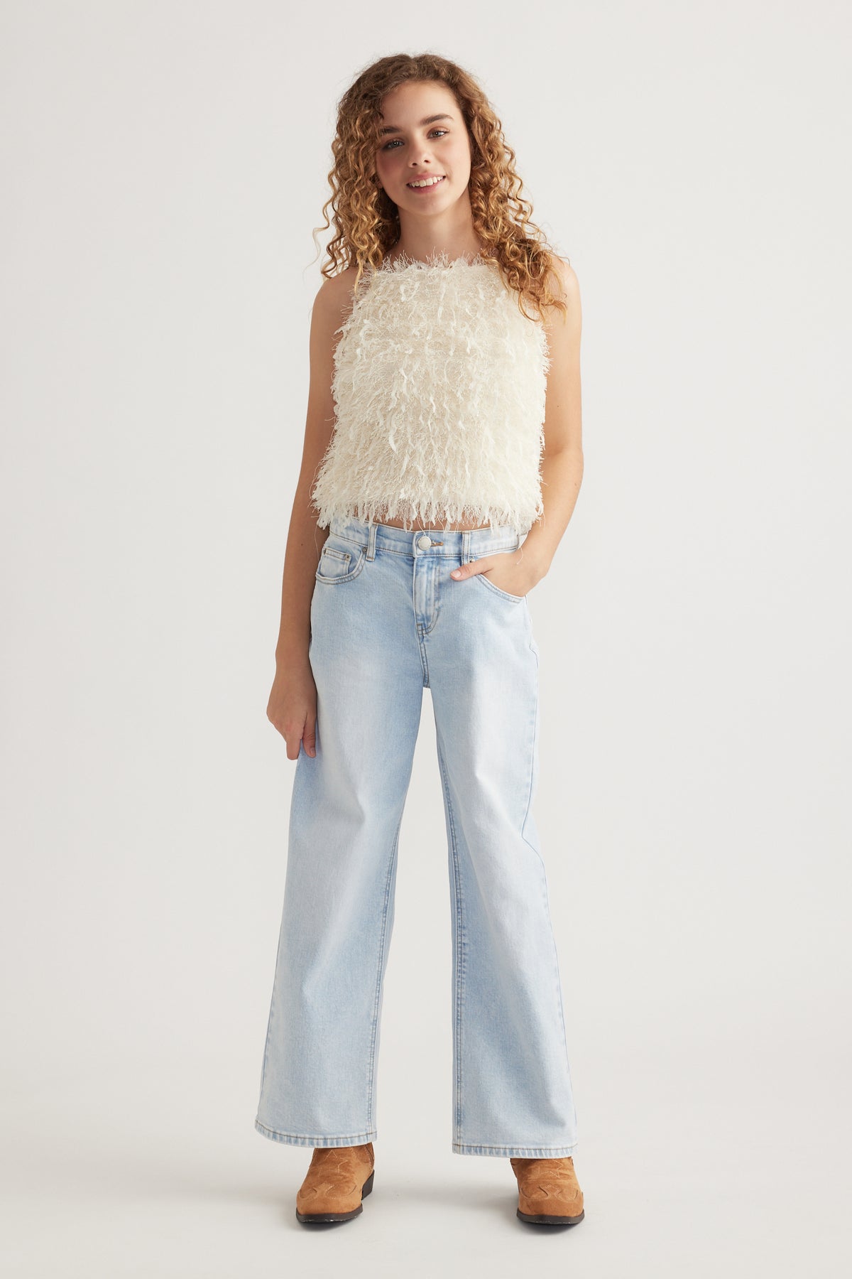 Girl wearing a cream textured sleeveless top with fringe, light blue wide-leg jeans and brown ankle boots