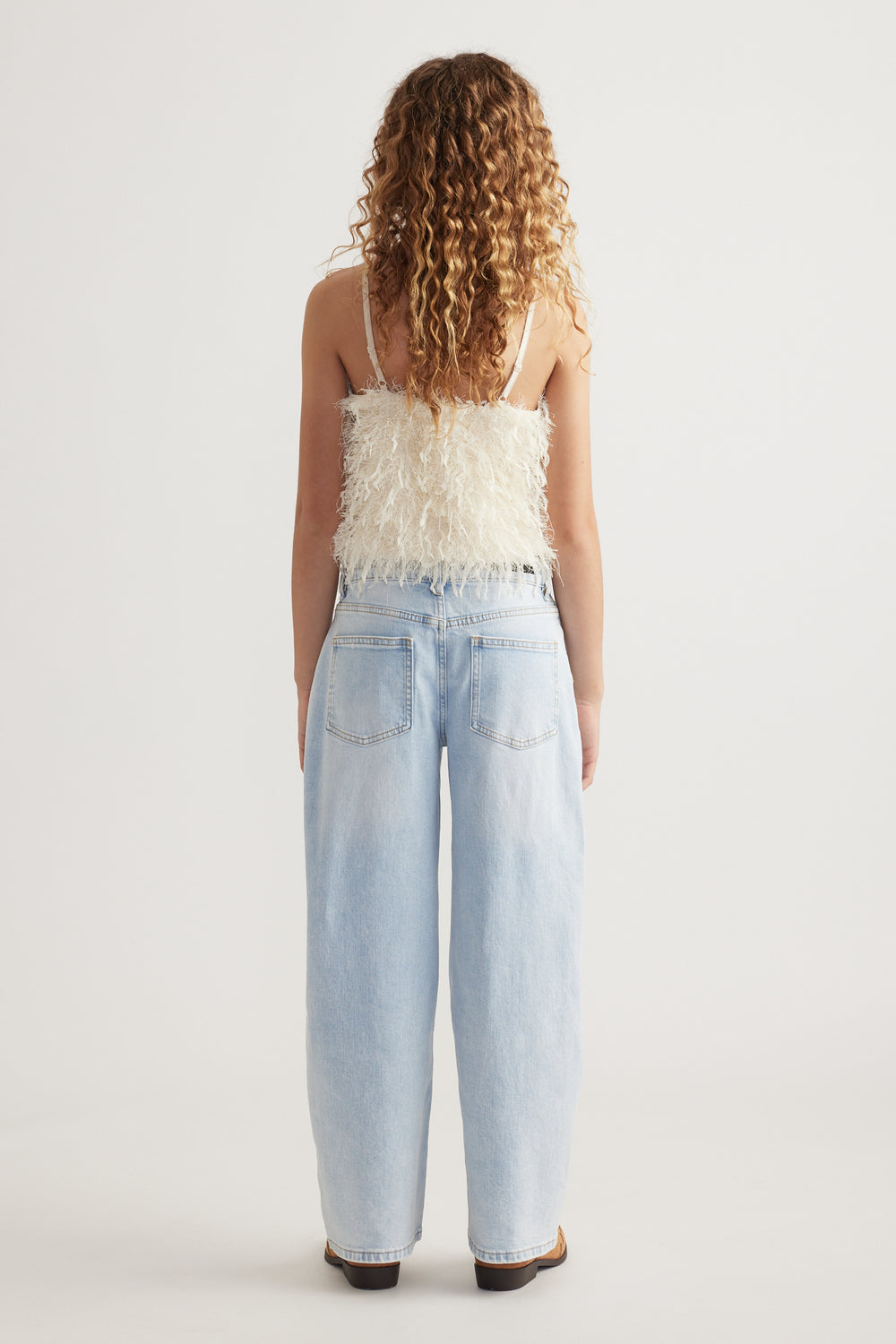 Back view of a woman wearing a textured cream camisole with thin straps and light blue wide leg jeans