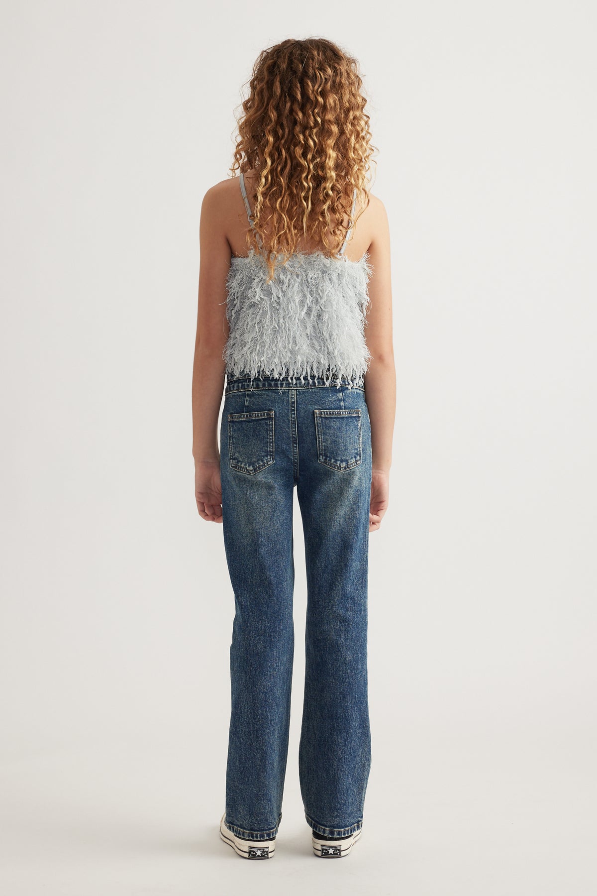 Back view of a girl wearing a textured sleeveless top with thin straps and blue straight-leg jeans