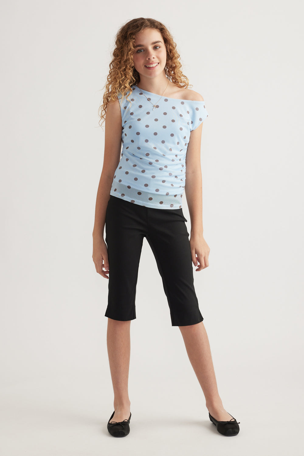 Girl wearing a light blue polka dot asymmetric top with black cropped pants and ballet flats