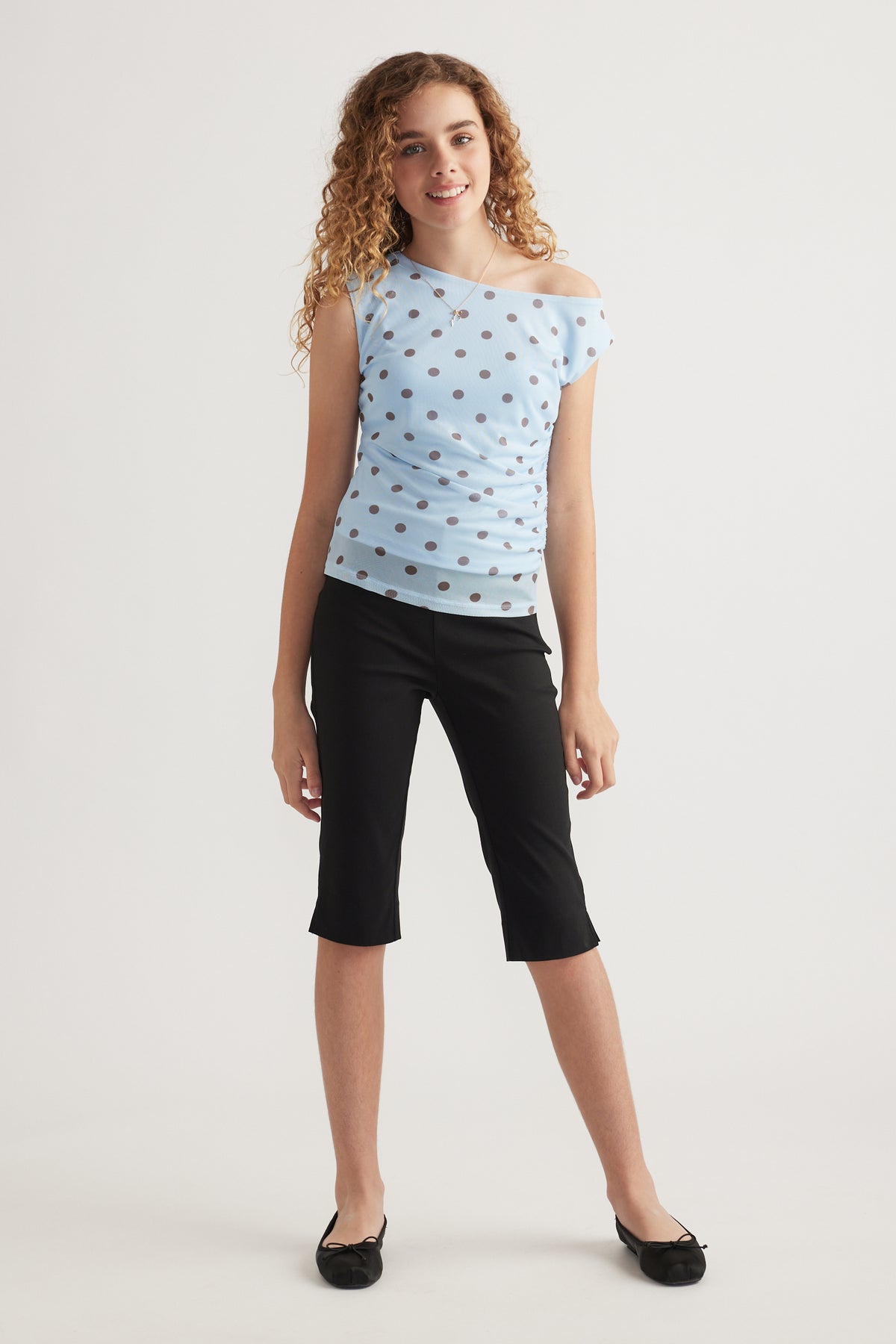 Girl wearing a light blue polka dot asymmetric top with black cropped pants and ballet flats