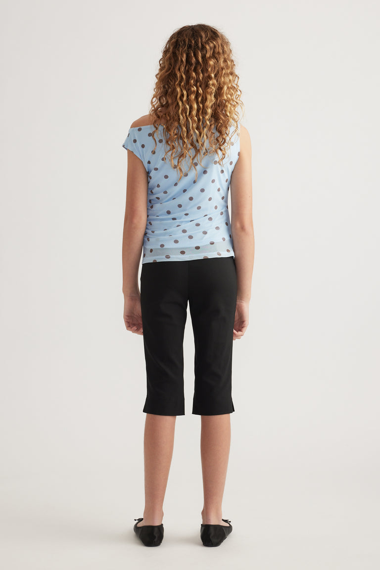 Girl viewed from behind wearing a light blue polka dot asymmetric top with black cropped pants and flats