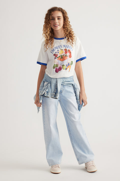 Girl wearing an oversized white graphic tee with blue trim, light wash wide leg jeans and a denim jacket tied at the waist