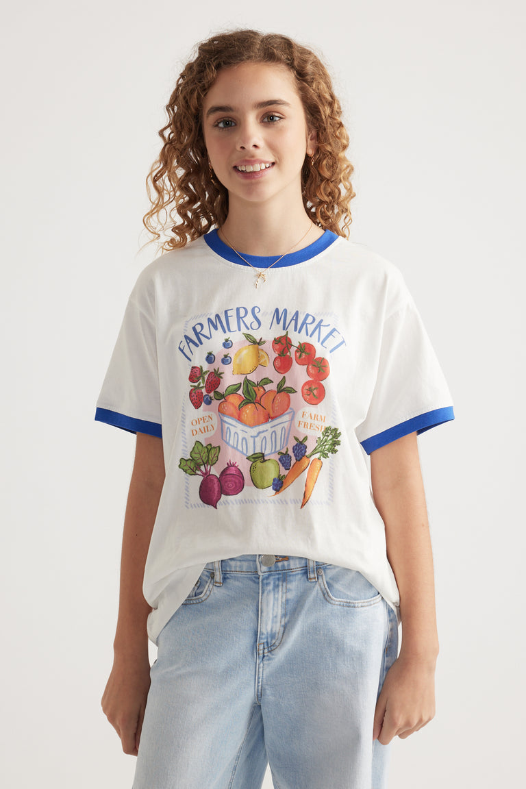 Girl wearing an oversized white graphic tee with blue trim and light wash jeans