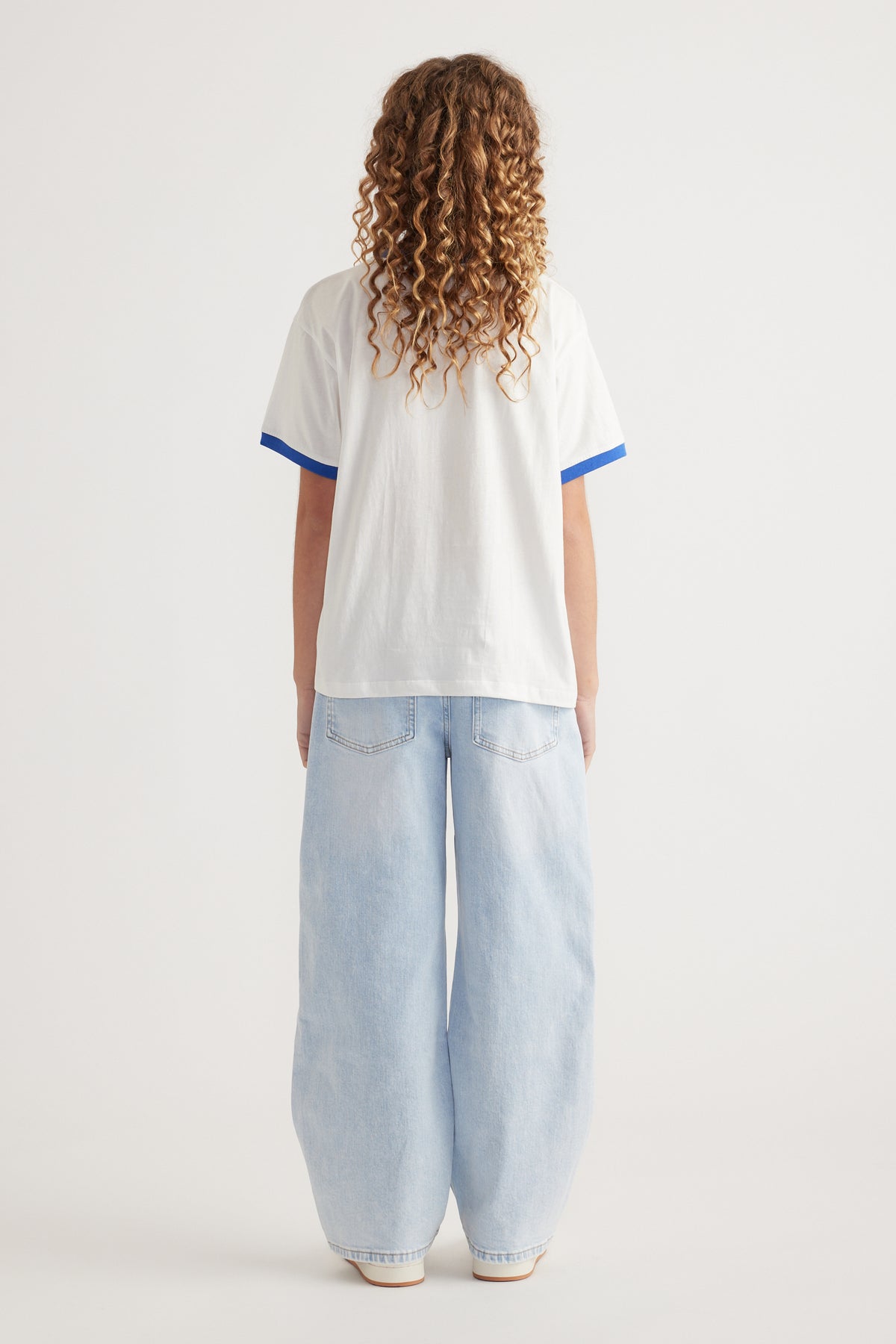 Back view of girl wearing an oversized white tee with blue trim and light wash wide leg jeans