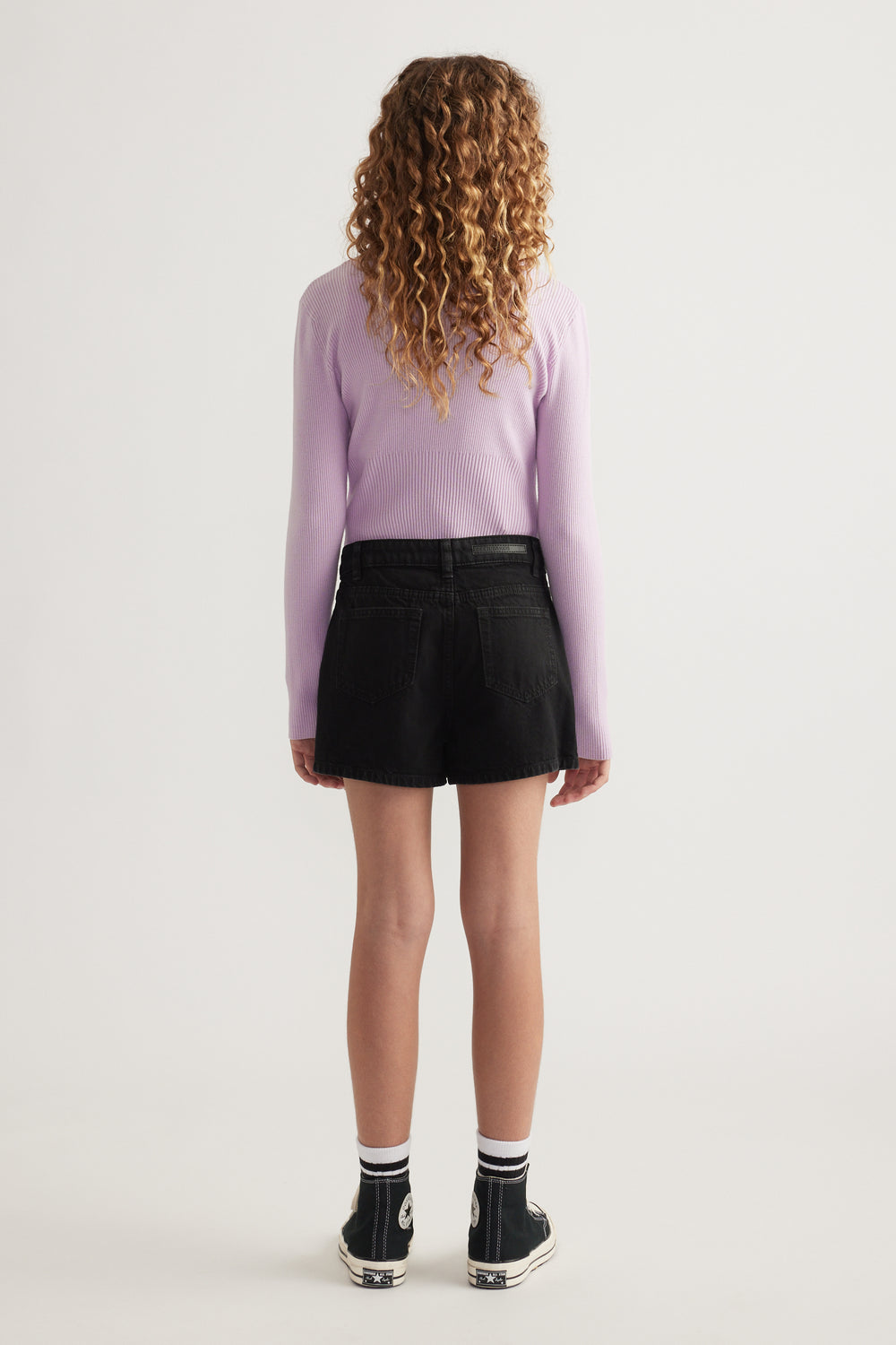 Girl wearing a black skort with a lilac ribbed top and sneakers, shown from the back