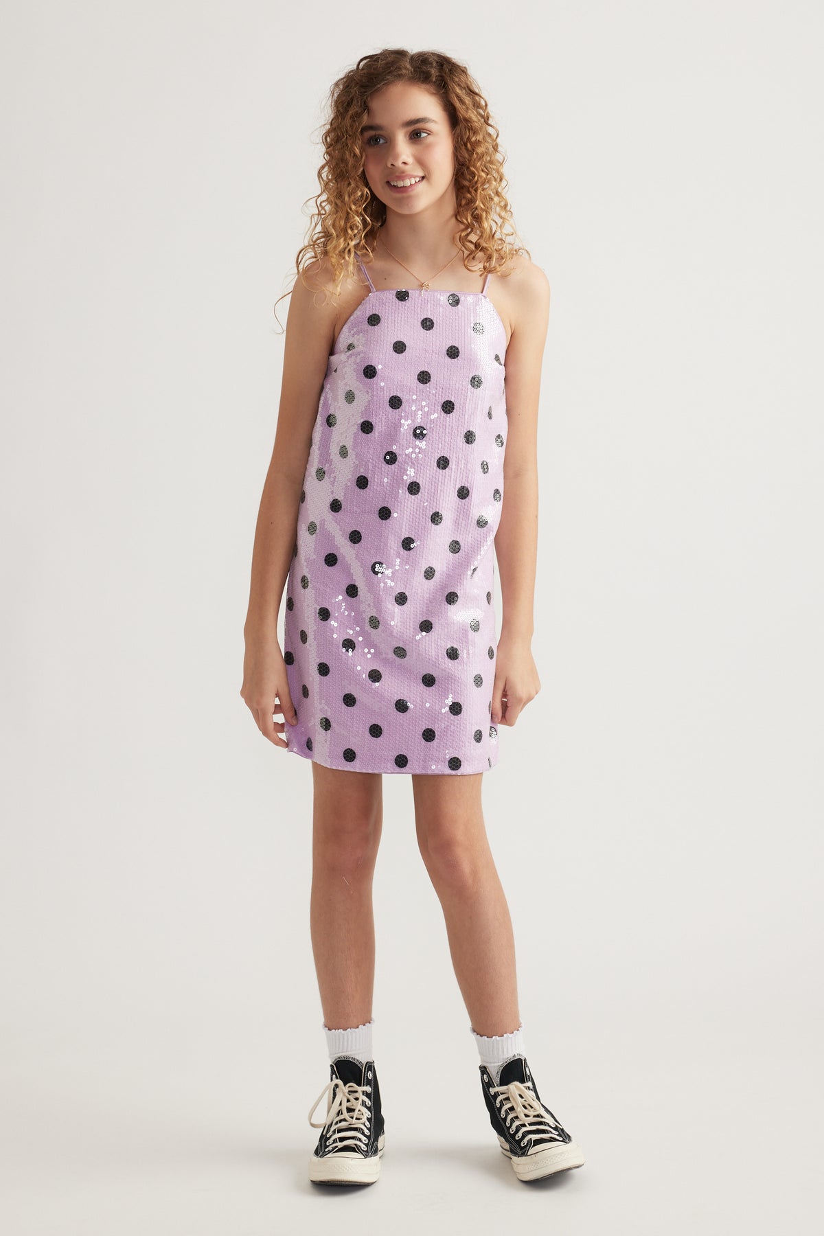 Girl wearing a lavender sequin mini dress with black polka dots and sneakers