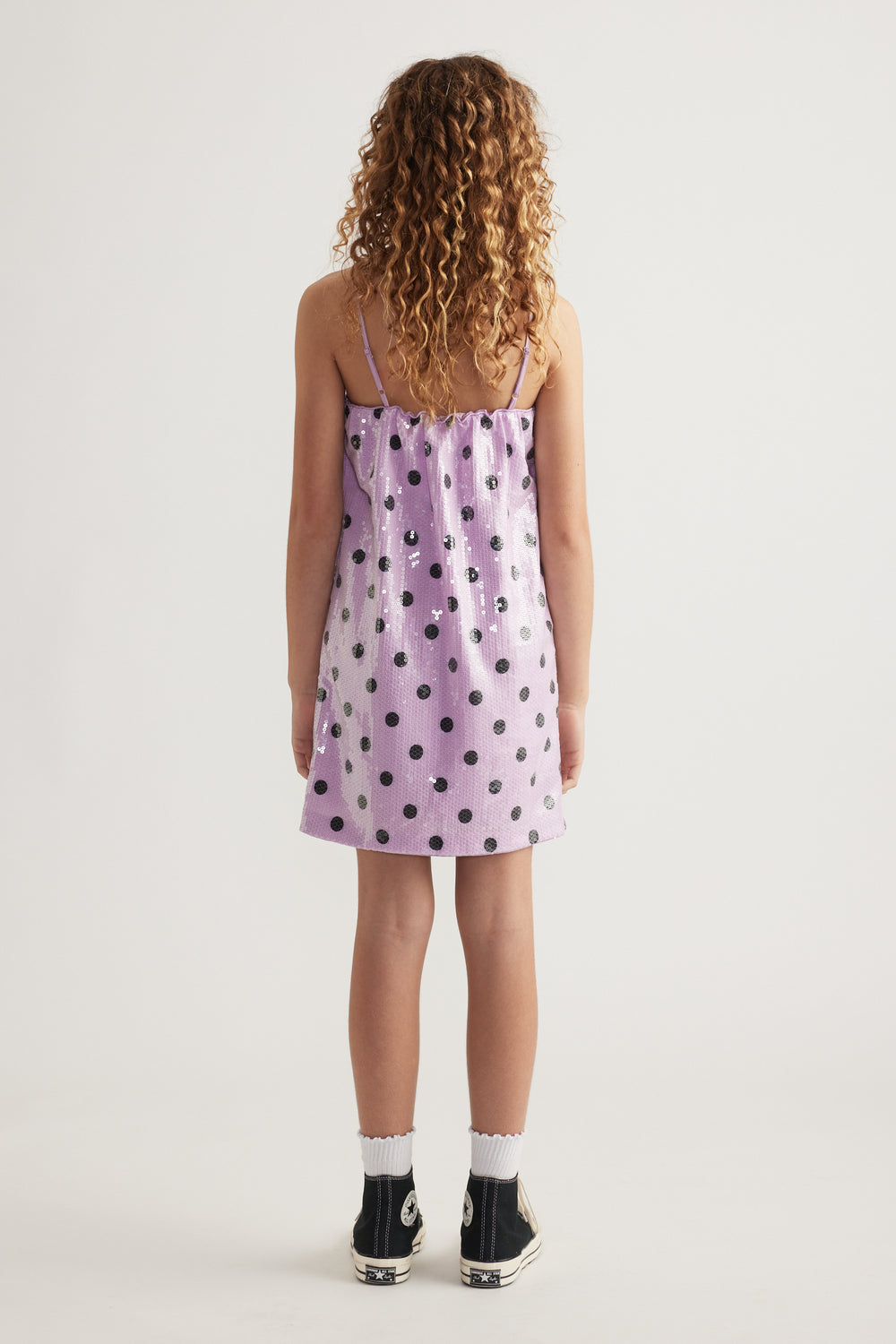 Back view of a girl wearing a lilac sequin mini dress with thin straps and black polka dots