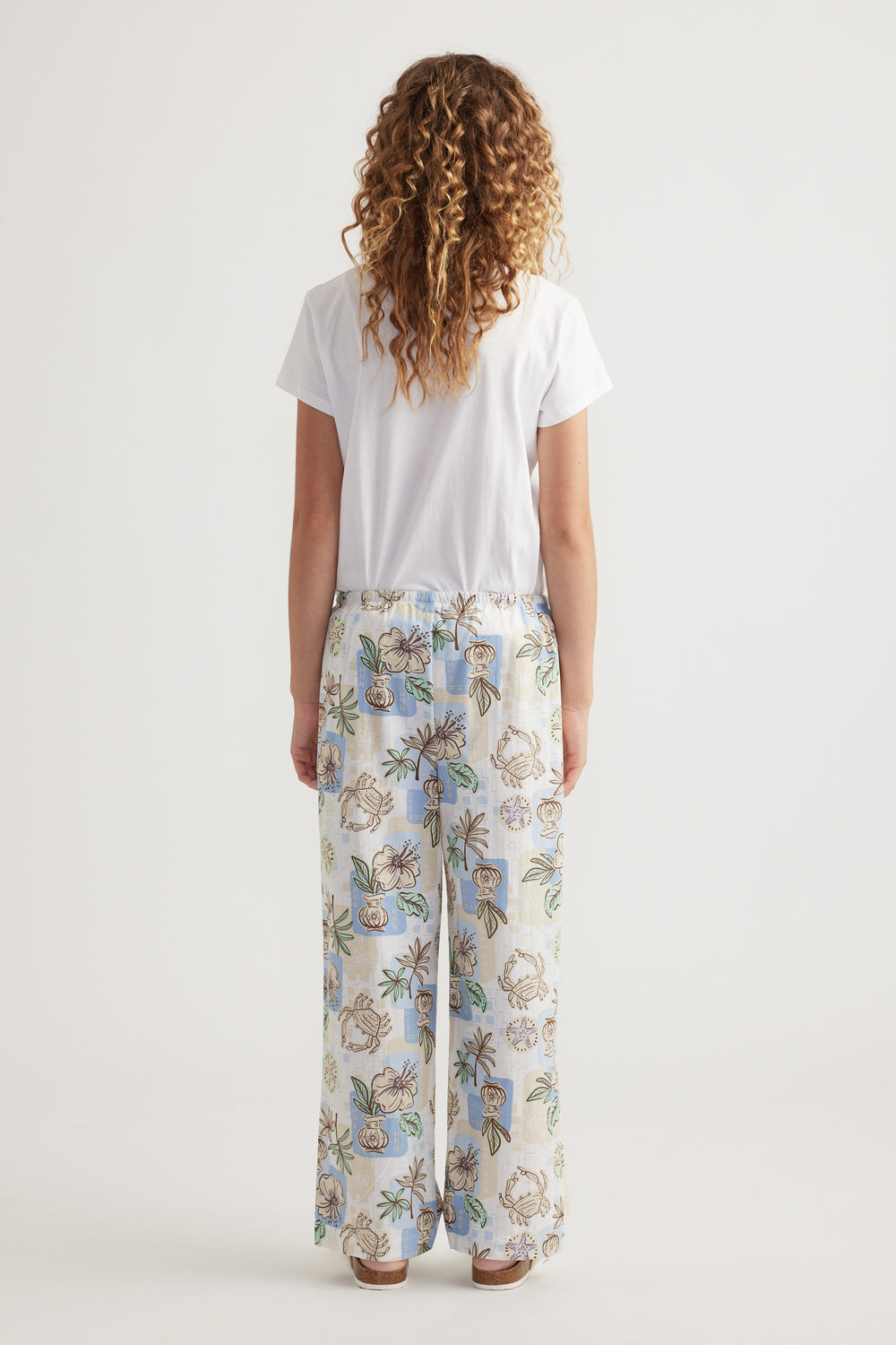 Girl viewed from behind wearing a white tee with floral wide-leg pants and sandals