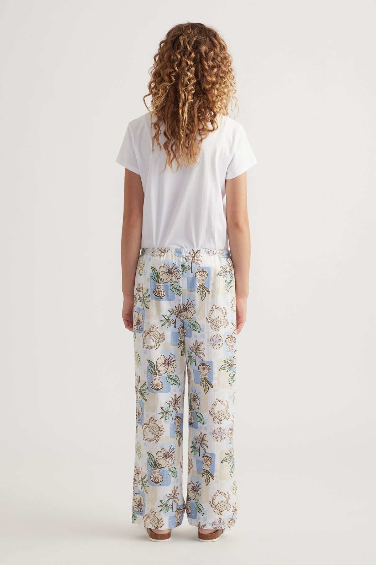 Girl viewed from behind wearing a white tee with floral wide-leg pants and sandals