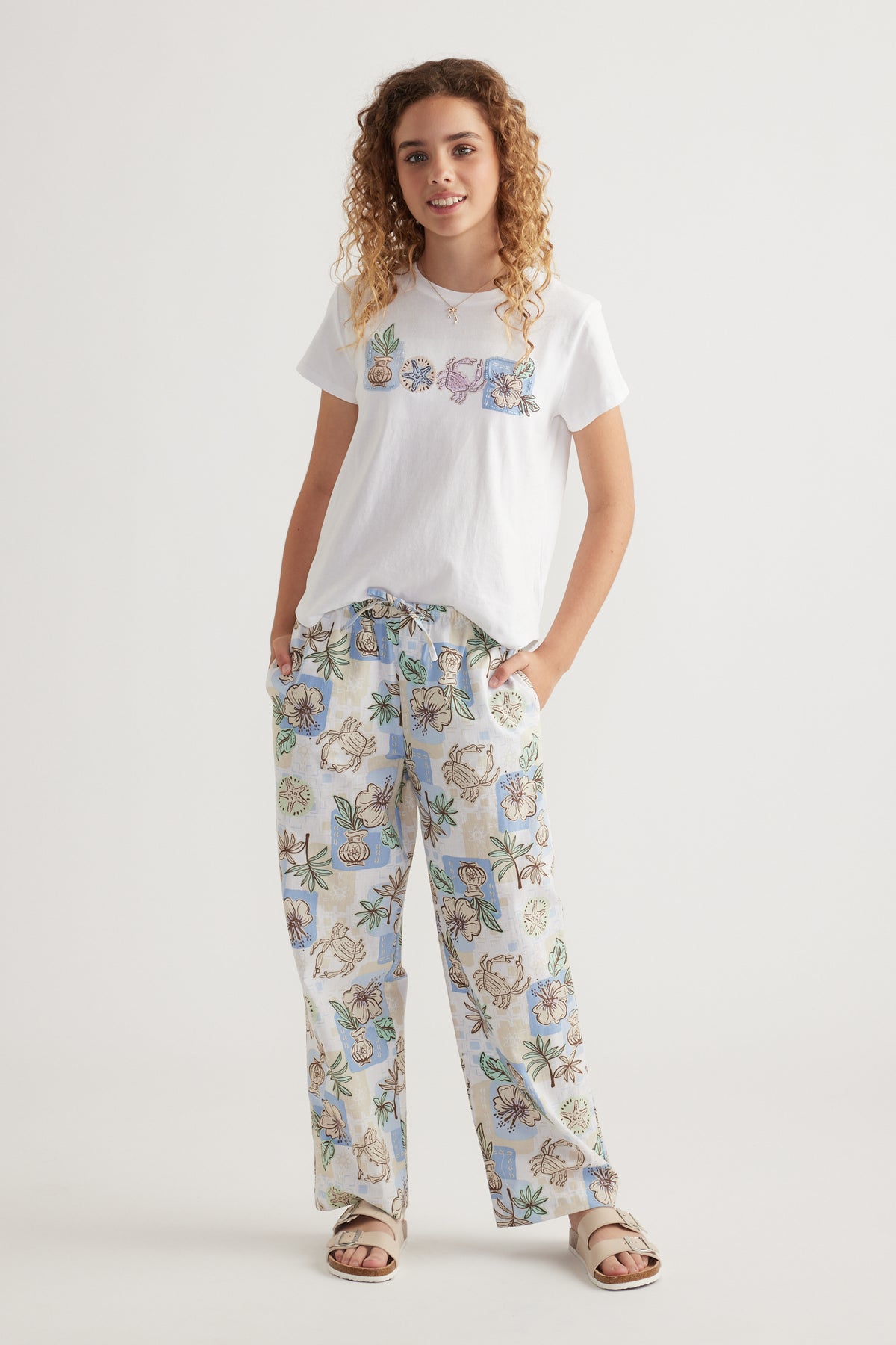 Girl wearing floral wide leg pants with a white graphic tee and sandals
