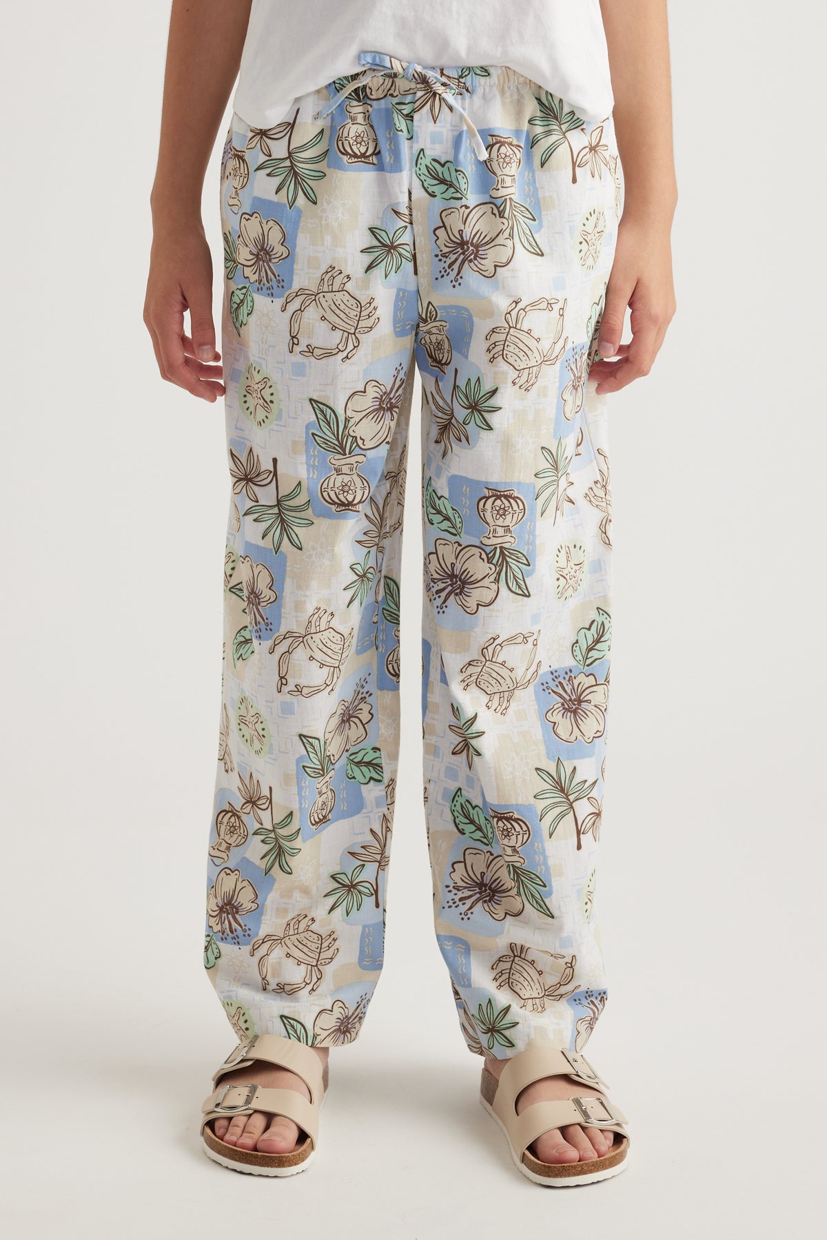 Model wearing full length floral wide leg pants with an elastic waist and neutral sandals