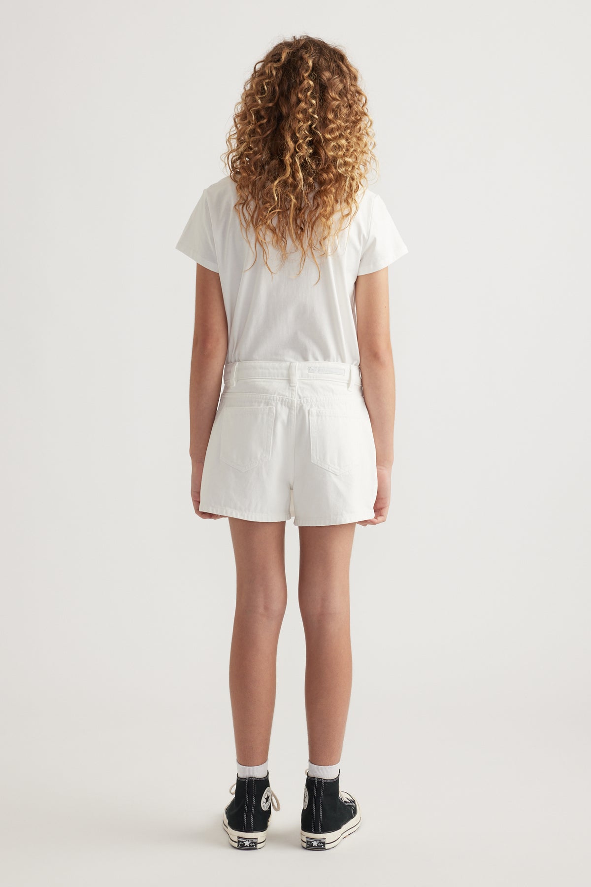 Girl wearing a white tee with a white denim skort and black sneakers, viewed from behind