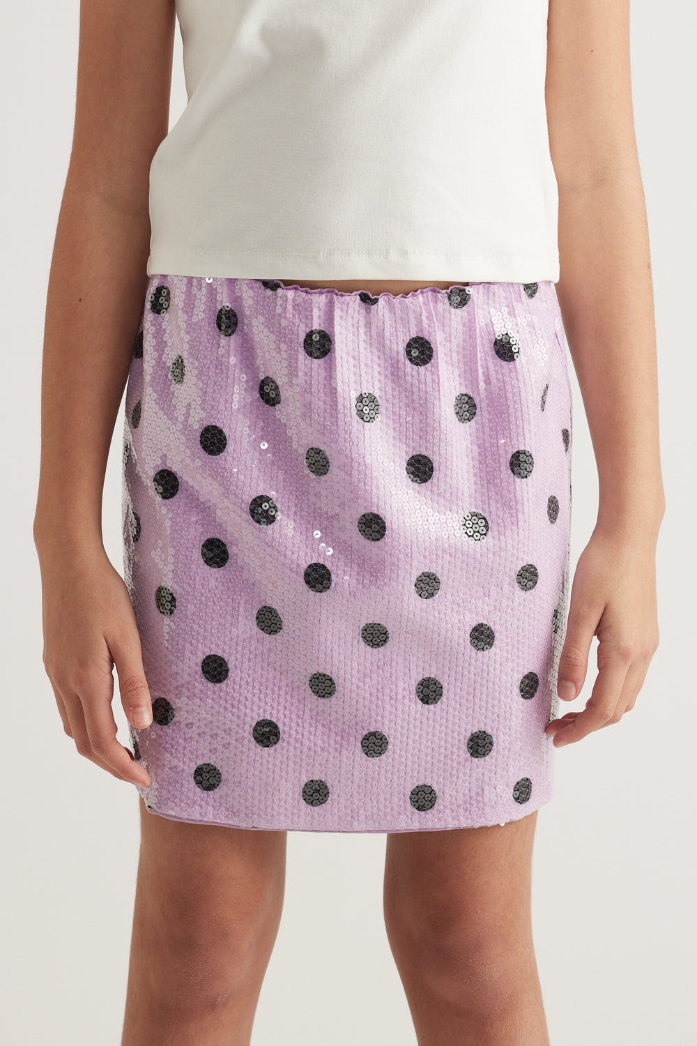 Girl wearing a lilac sequin mini skirt with black polka dots and an elastic waist