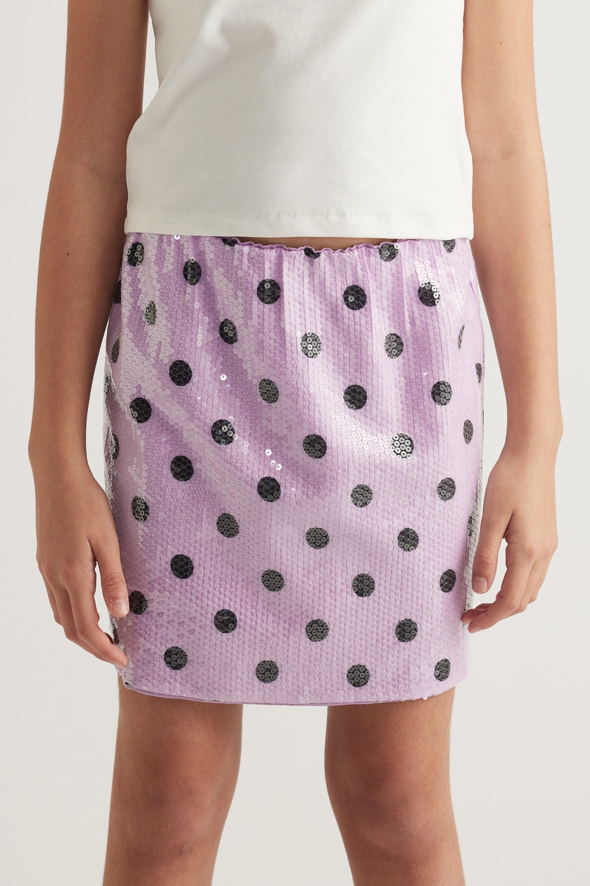Girl wearing a lilac sequin mini skirt with black polka dots and an elastic waist
