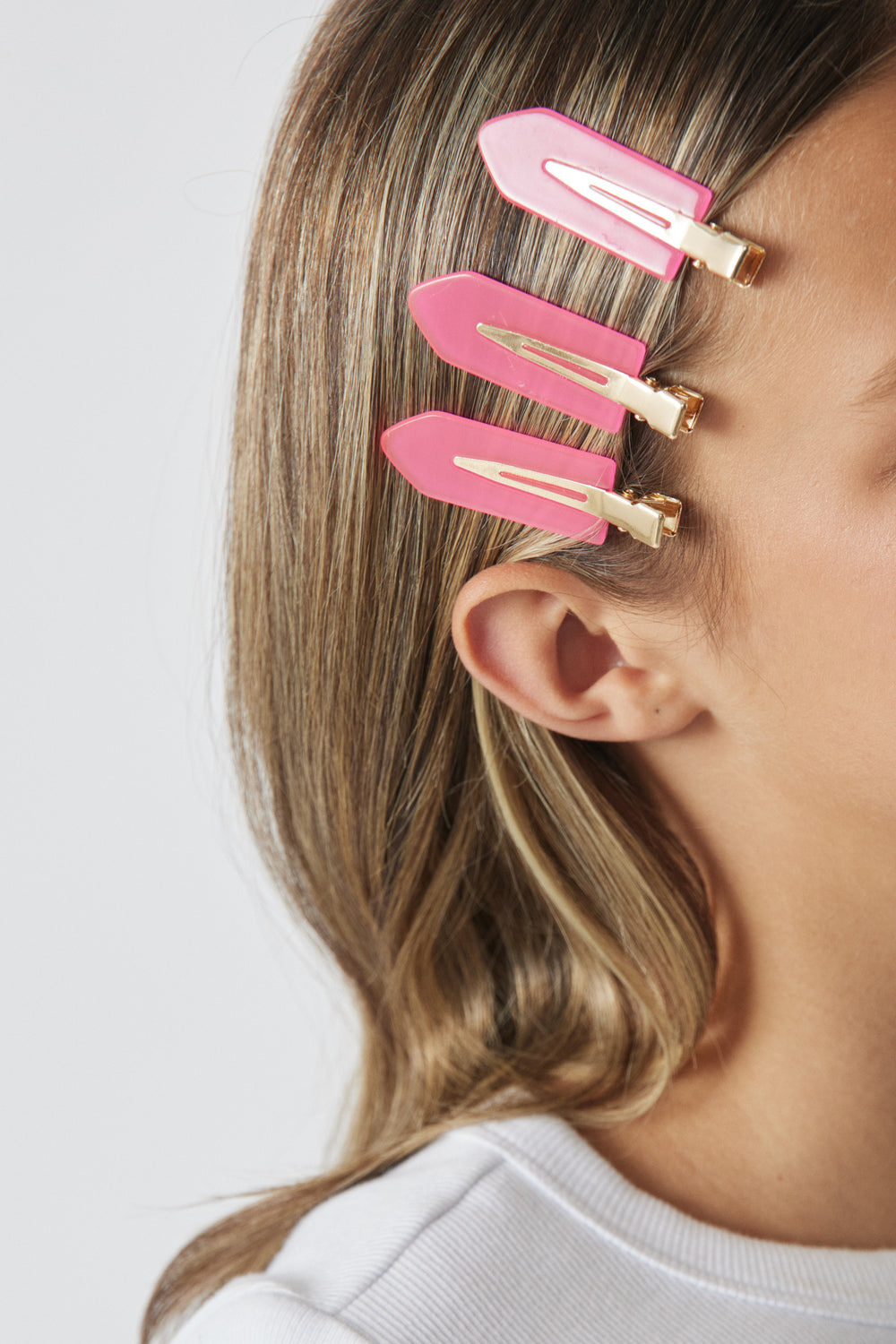 Three pink hair clips with gold accents worn on the side of a girl's light brown hair, close-up view.