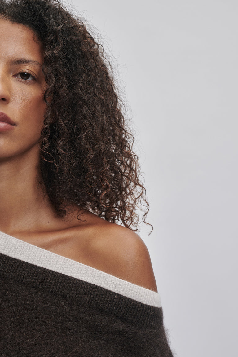 Close-up of woman with curly hair wearing a soft wool jumper with a contrasting off-shoulder neckline detail