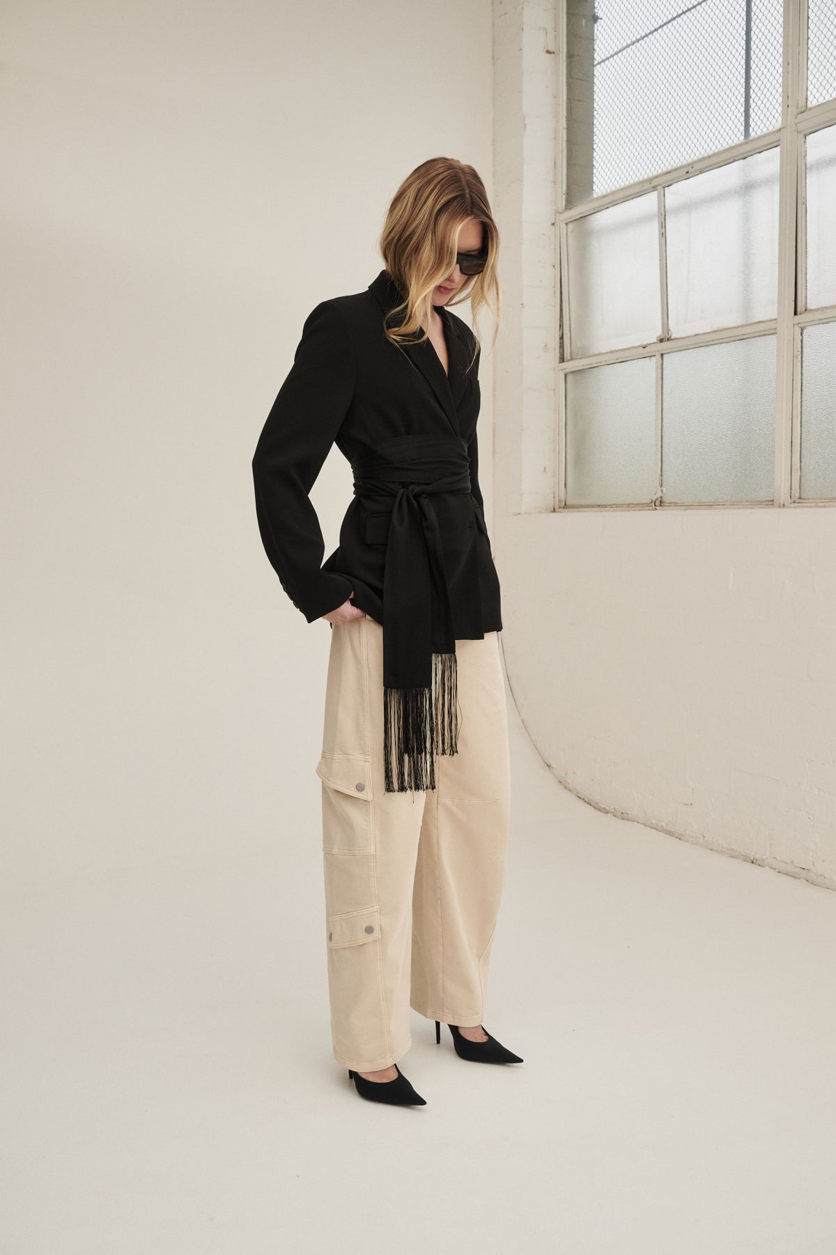 Woman wearing cream barrel leg cargo pants with a black belted blazer and pointed flats