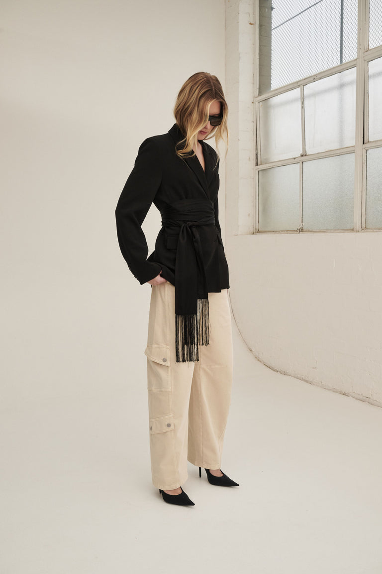 Woman wearing cream barrel leg cargo pants with a black belted blazer and pointed flats
