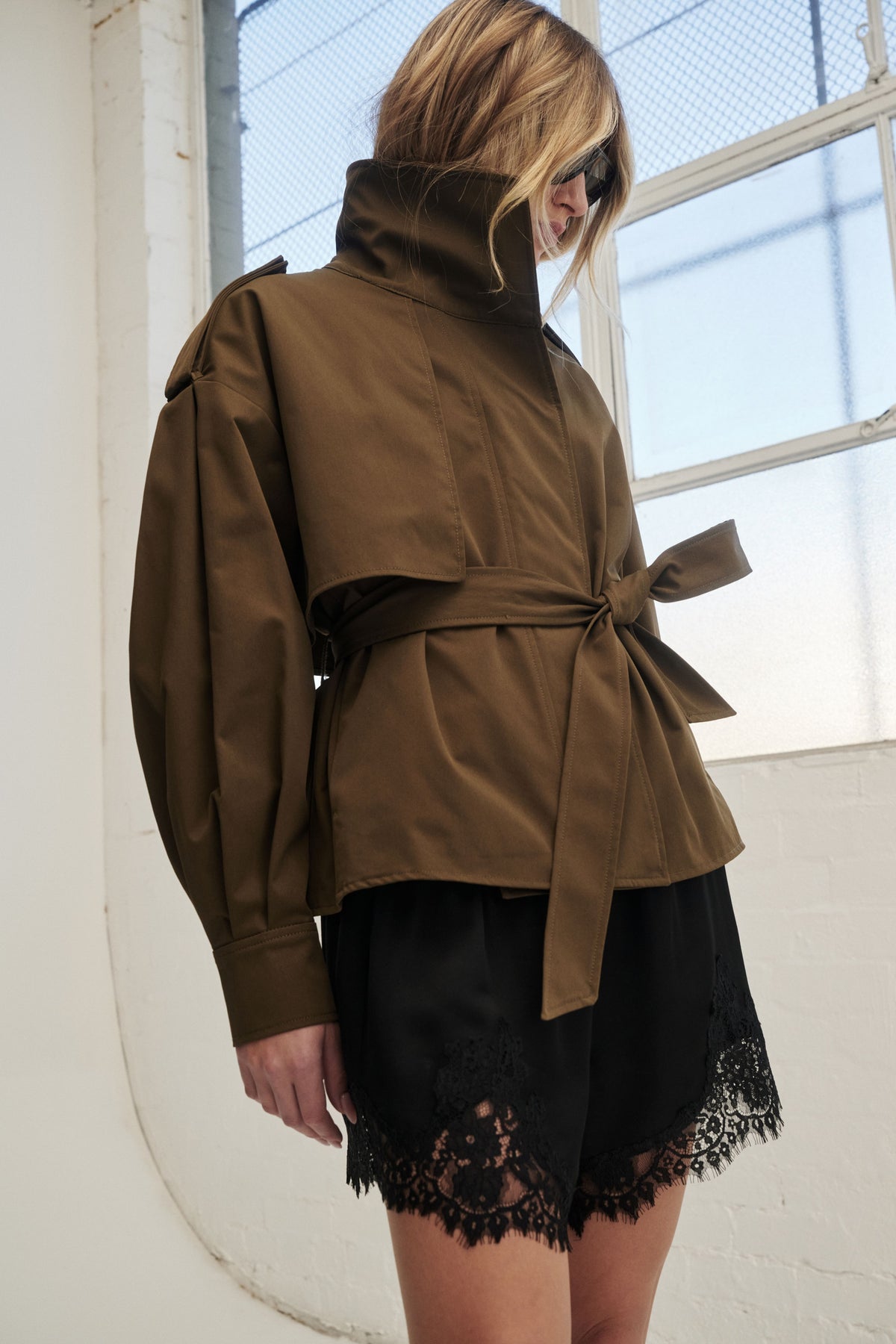 Woman wearing a brown cropped belted trench jacket over black lace trim shorts