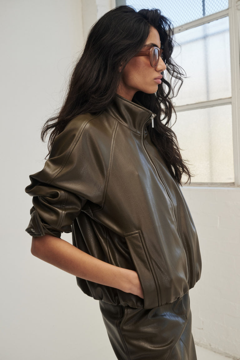 Woman wearing a dark brown faux leather bomber jacket with matching trousers and sunglasses