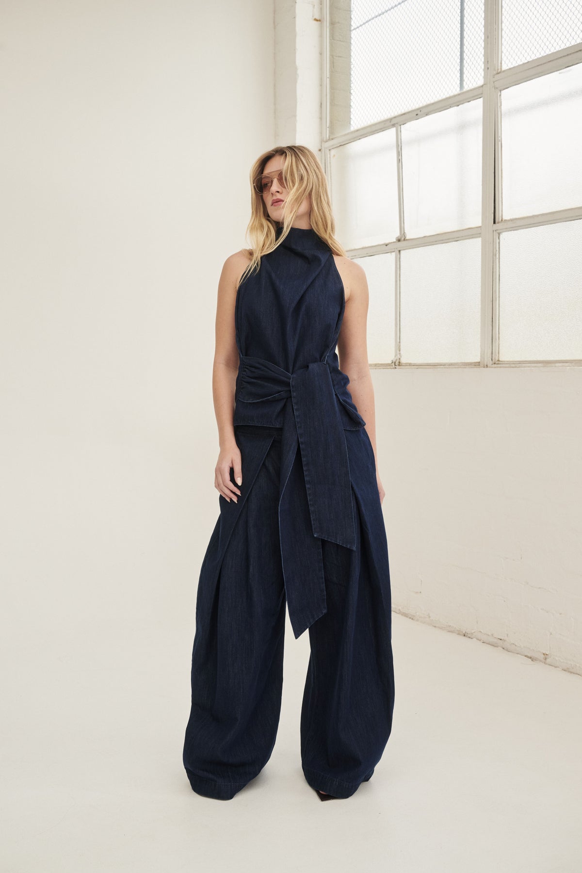 Woman wearing a navy sleeveless funnel neck top with waist tie and matching wide leg pants