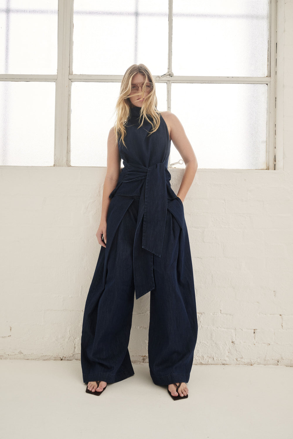 Woman wearing dark navy wide leg denim pants with a draped sleeveless top and black sandals