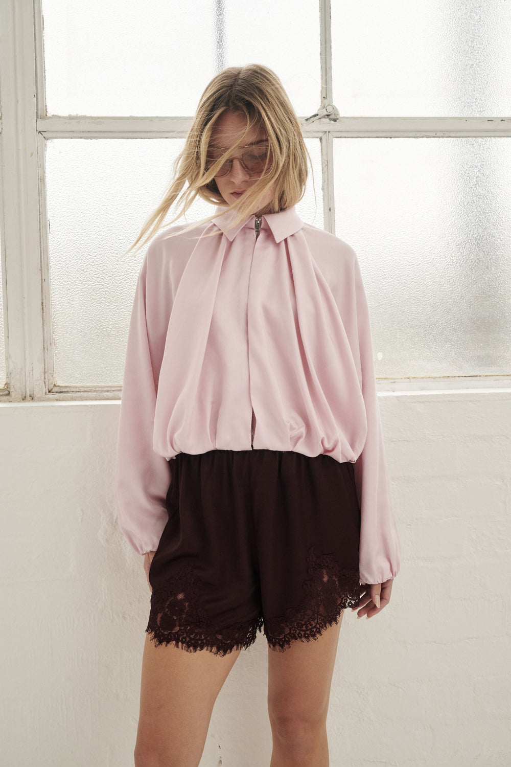 Woman wearing dark satin lace trim shorts with an oversized pink blouse
