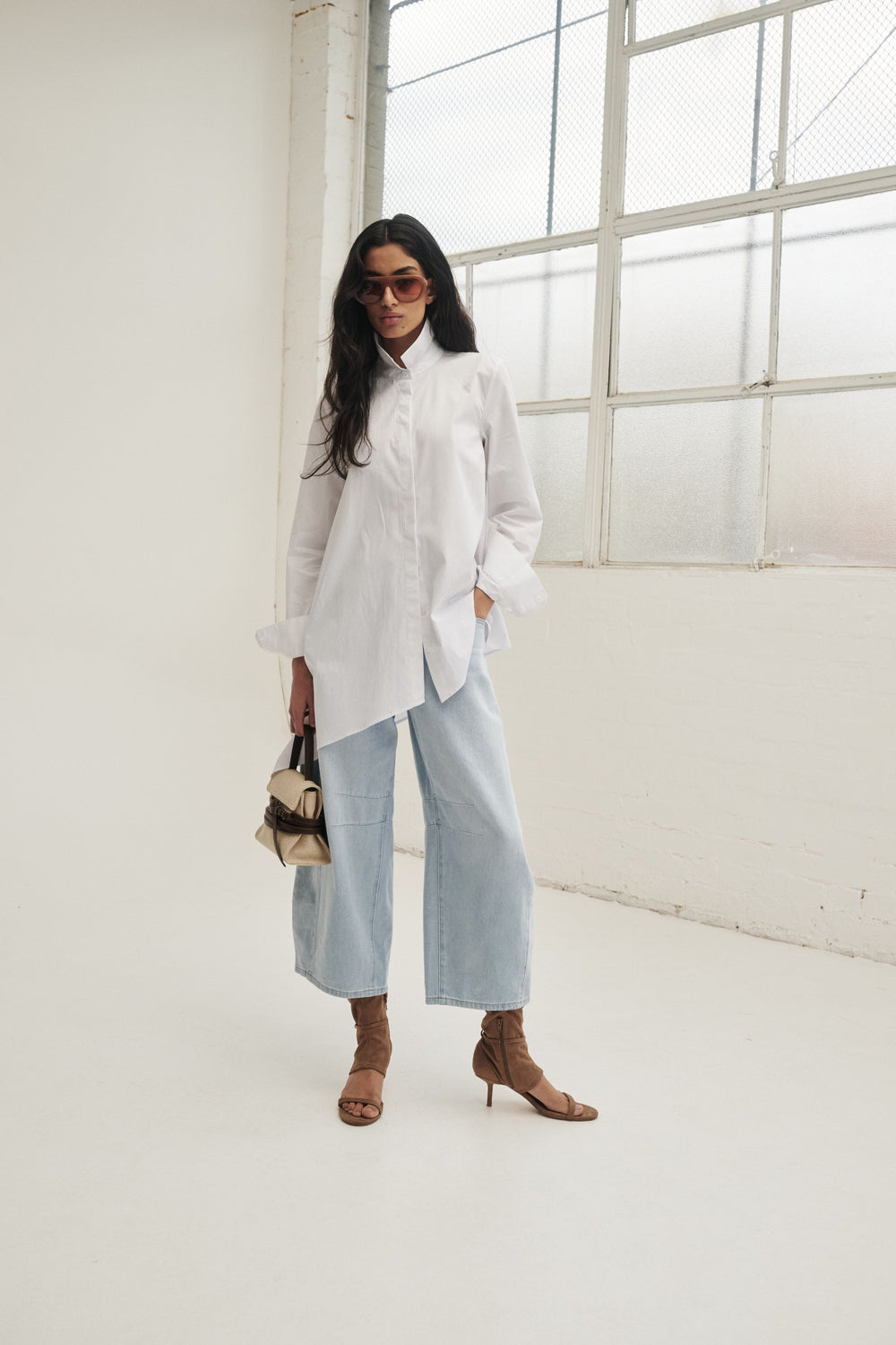 Woman in a white asymmetric button through shirt with light blue wide leg jeans and brown heeled sandals