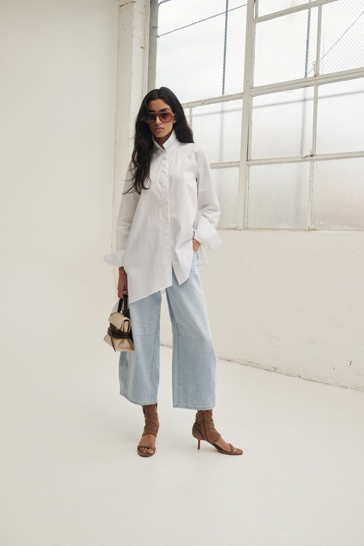 Woman in a white asymmetric button through shirt with light blue wide leg jeans and brown heeled sandals